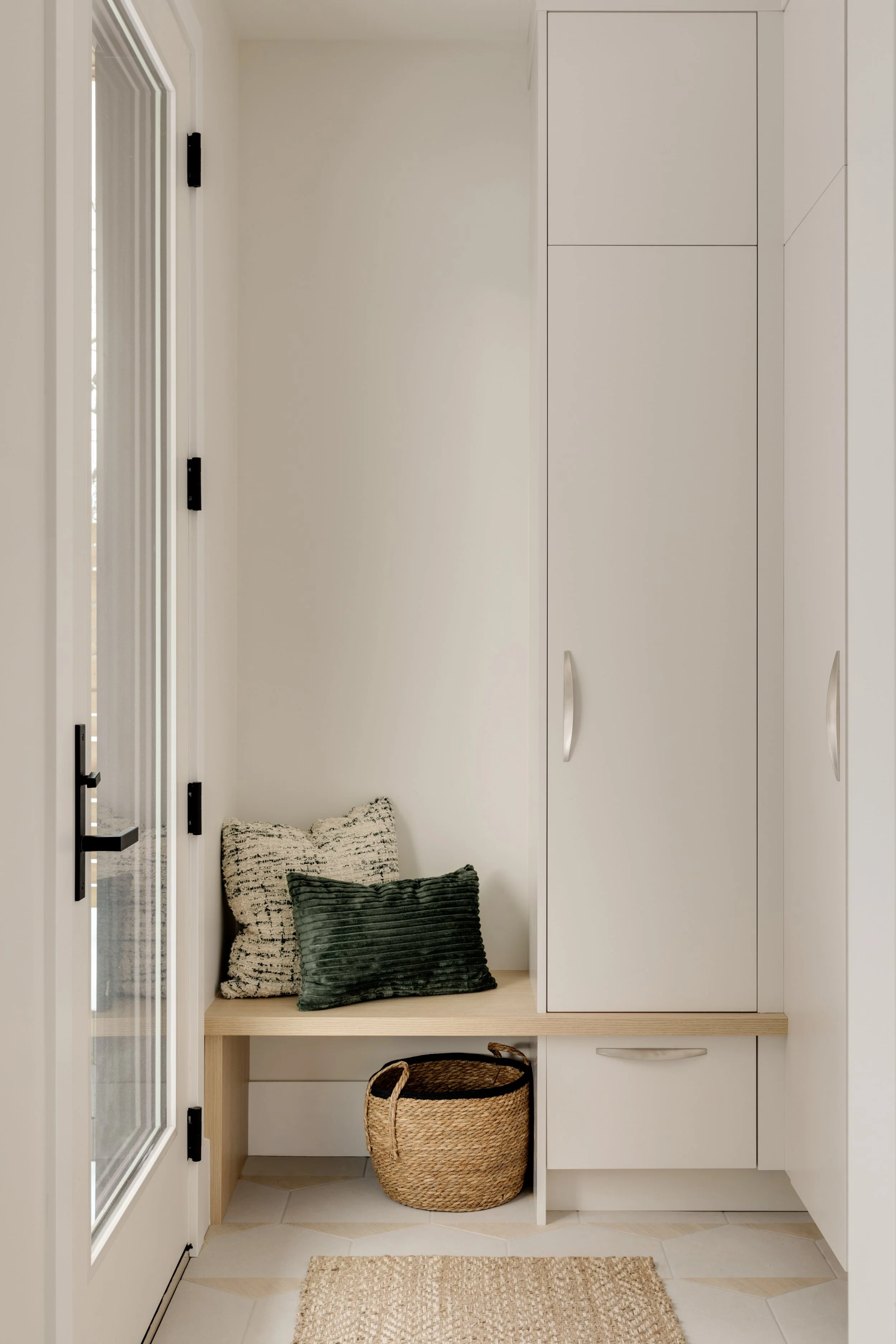 Entryway with white cabinetry, a bench with pillows, a woven basket, and a door with glass panels.