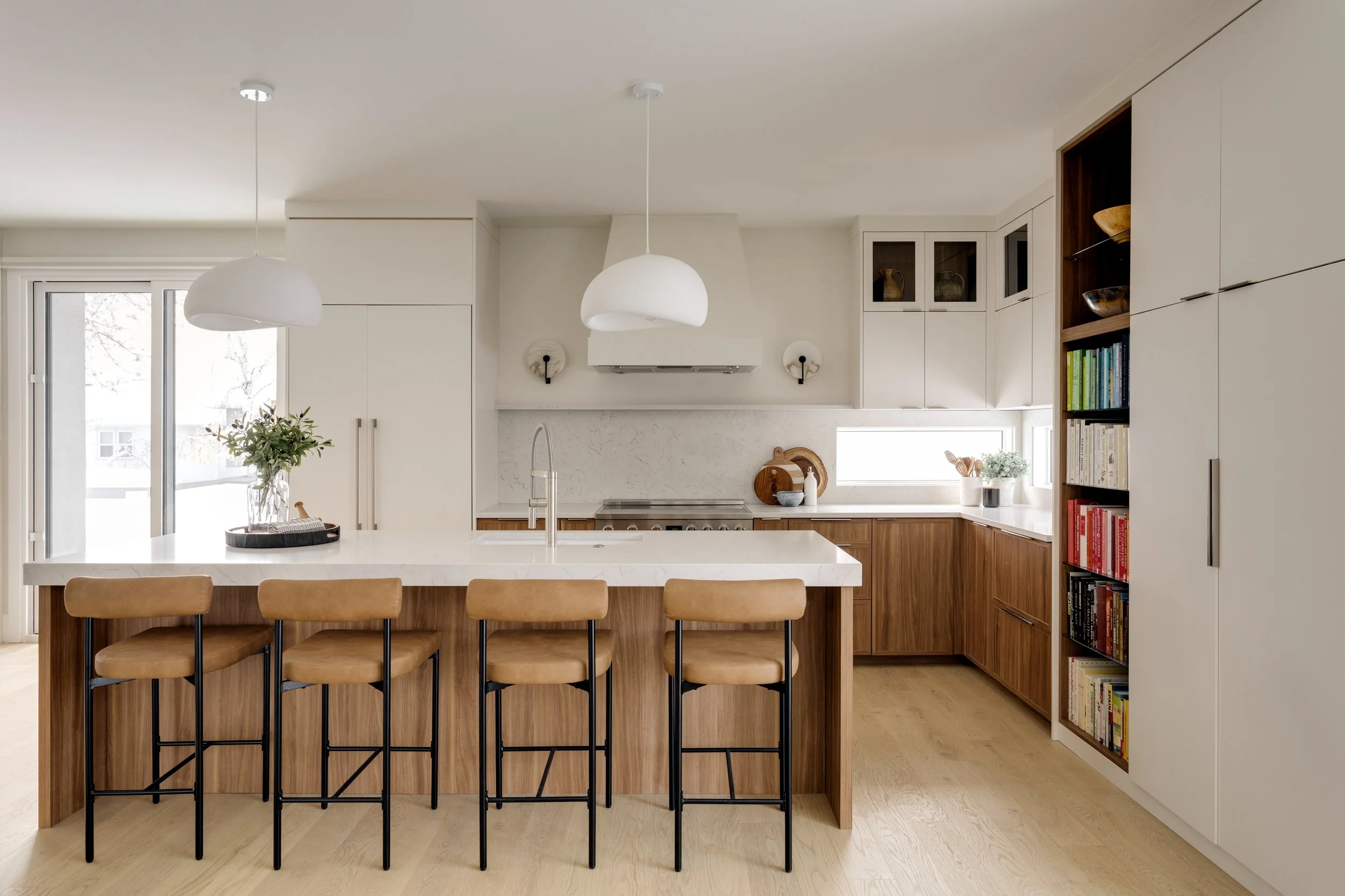 Modern kitchen with wooden island, light-colored cabinets, and a bookshelf with cookbooks and decorations.