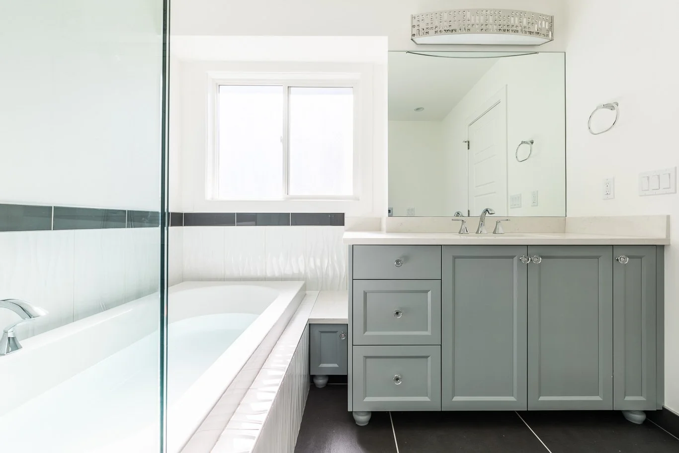 Bathroom with a bathtub, a window, a large mirror, and a gray vanity with a sink and drawers