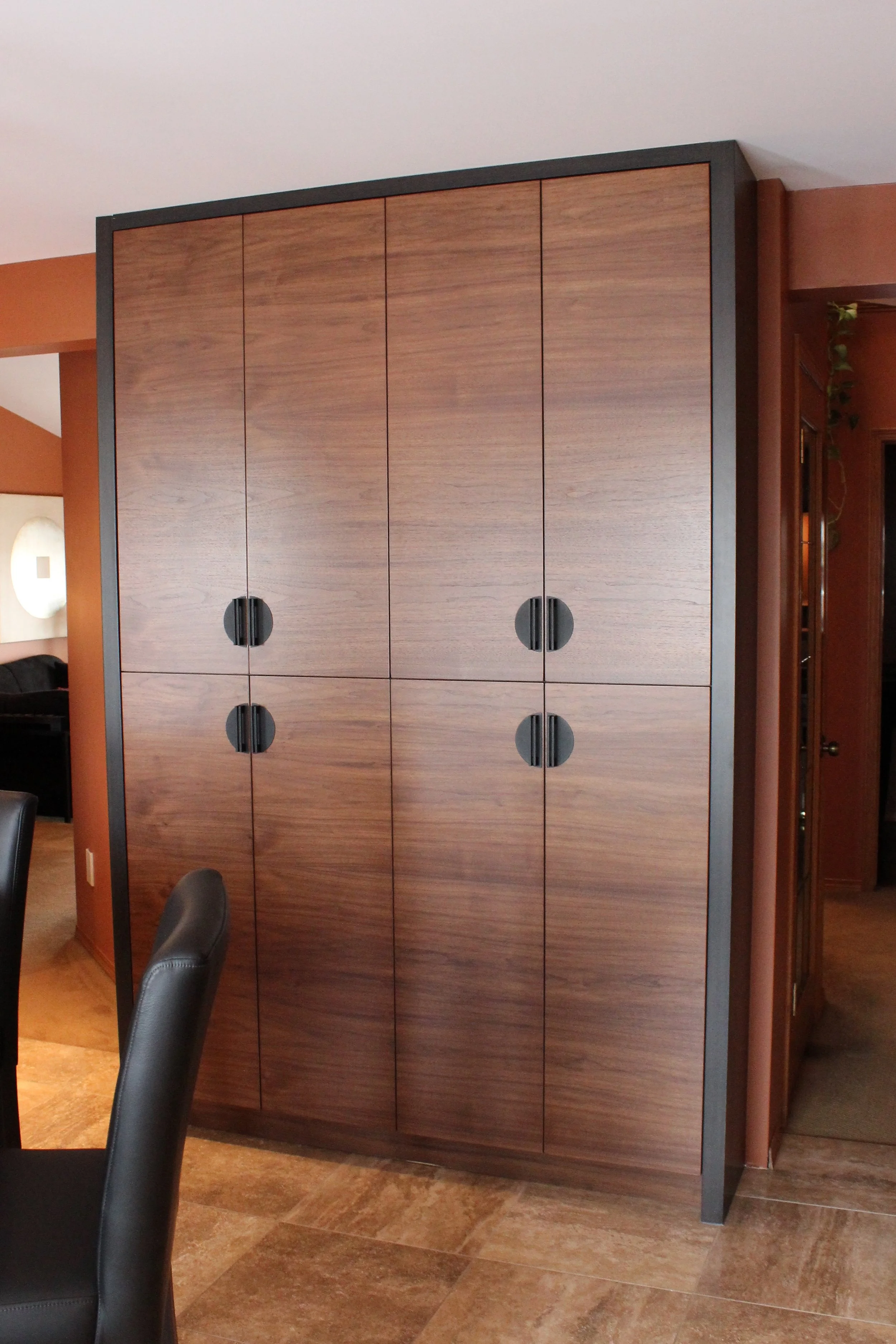 A wooden cabinet with black circular handles in an indoor space, with a brown wall and a doorway in the background.
