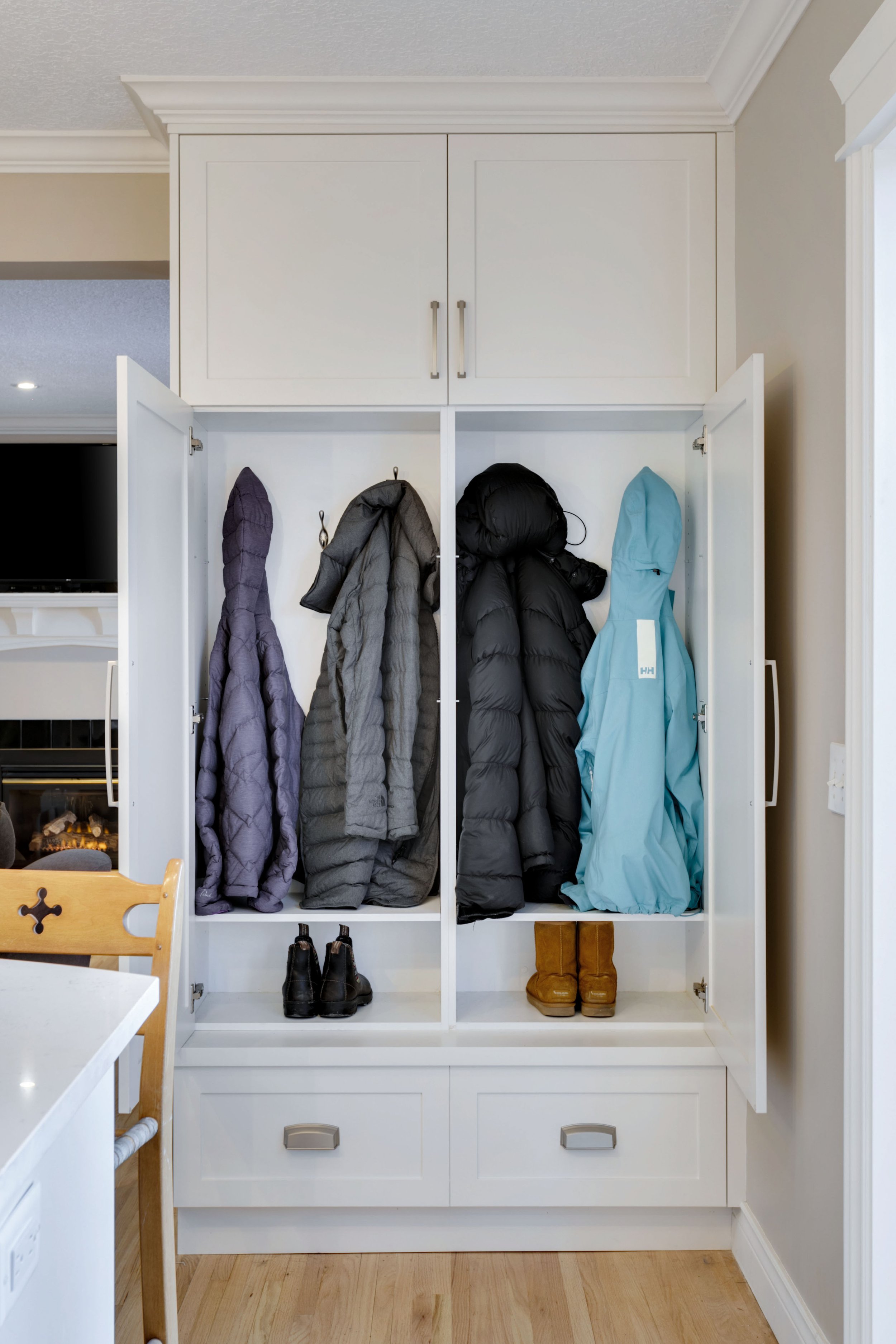 Open white coat closet with jackets hanging inside and shoes on bottom shelf.