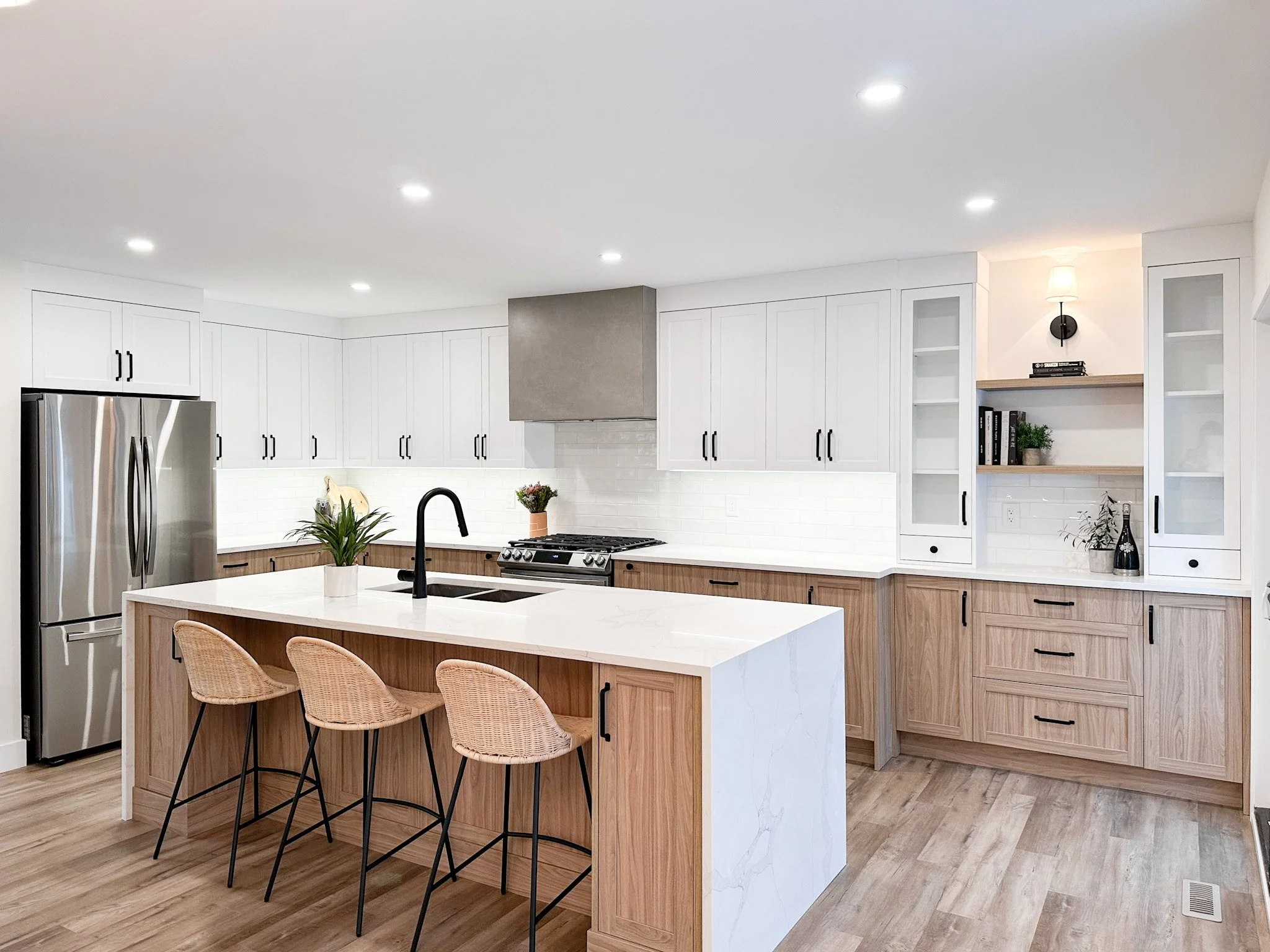 Modern kitchen with white cabinets, a kitchen island with a white countertop, bar stools, stainless steel refrigerator, black faucet, and open shelves with decorative items.