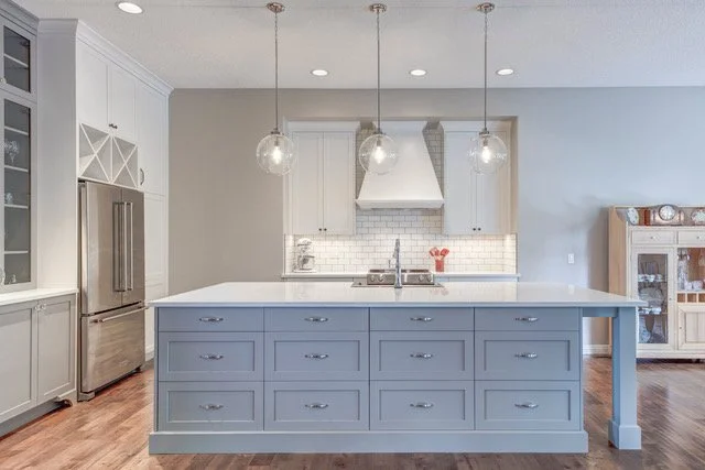 Modern kitchen with a blue island, white cabinets, stainless steel refrigerator, white subway tile backsplash, and pendant lights