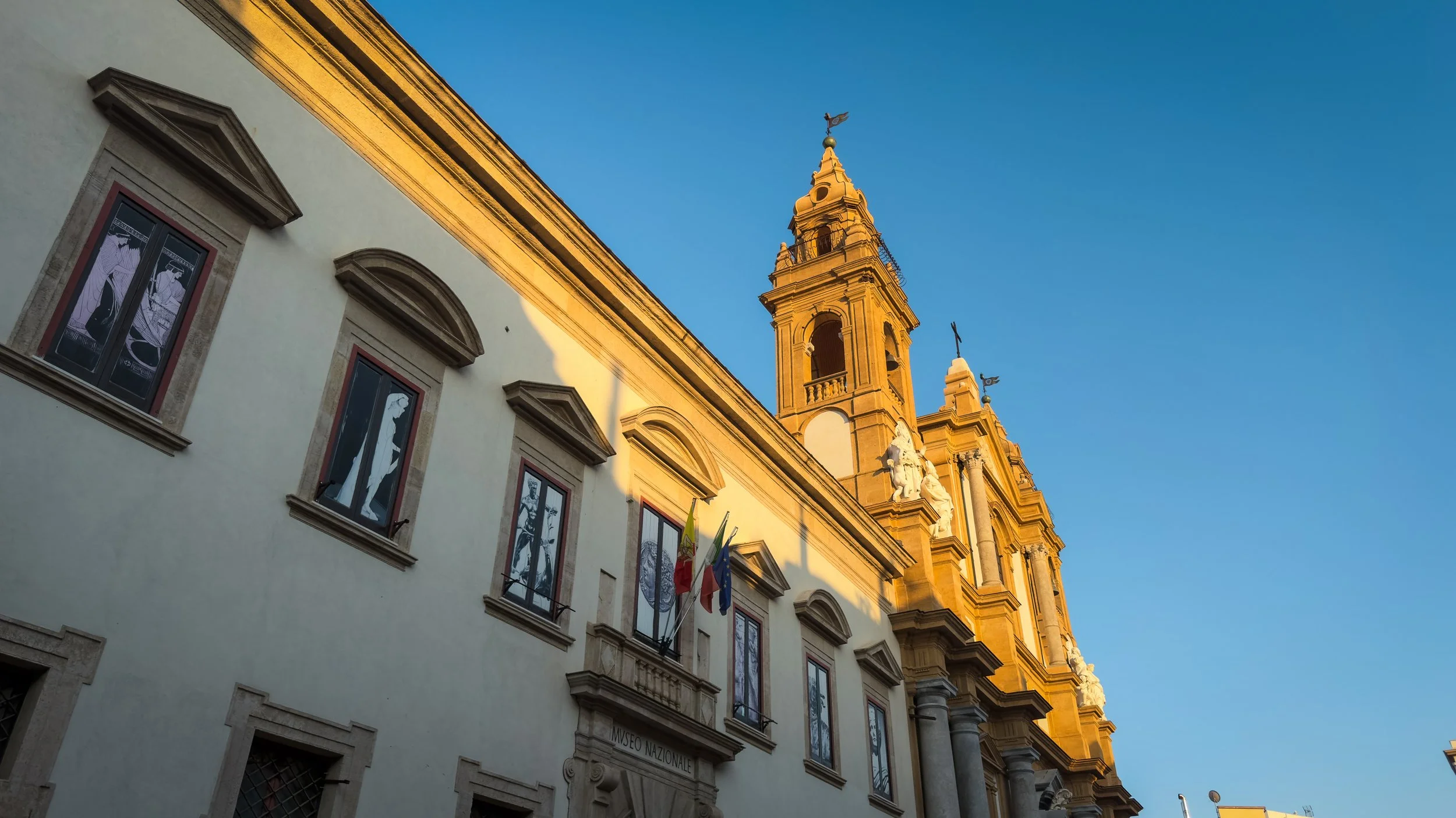 Exterior of Museo Archeologico Regionale Antonino Salinas in Palermo with the adjoining church tower rising against a blue sky.