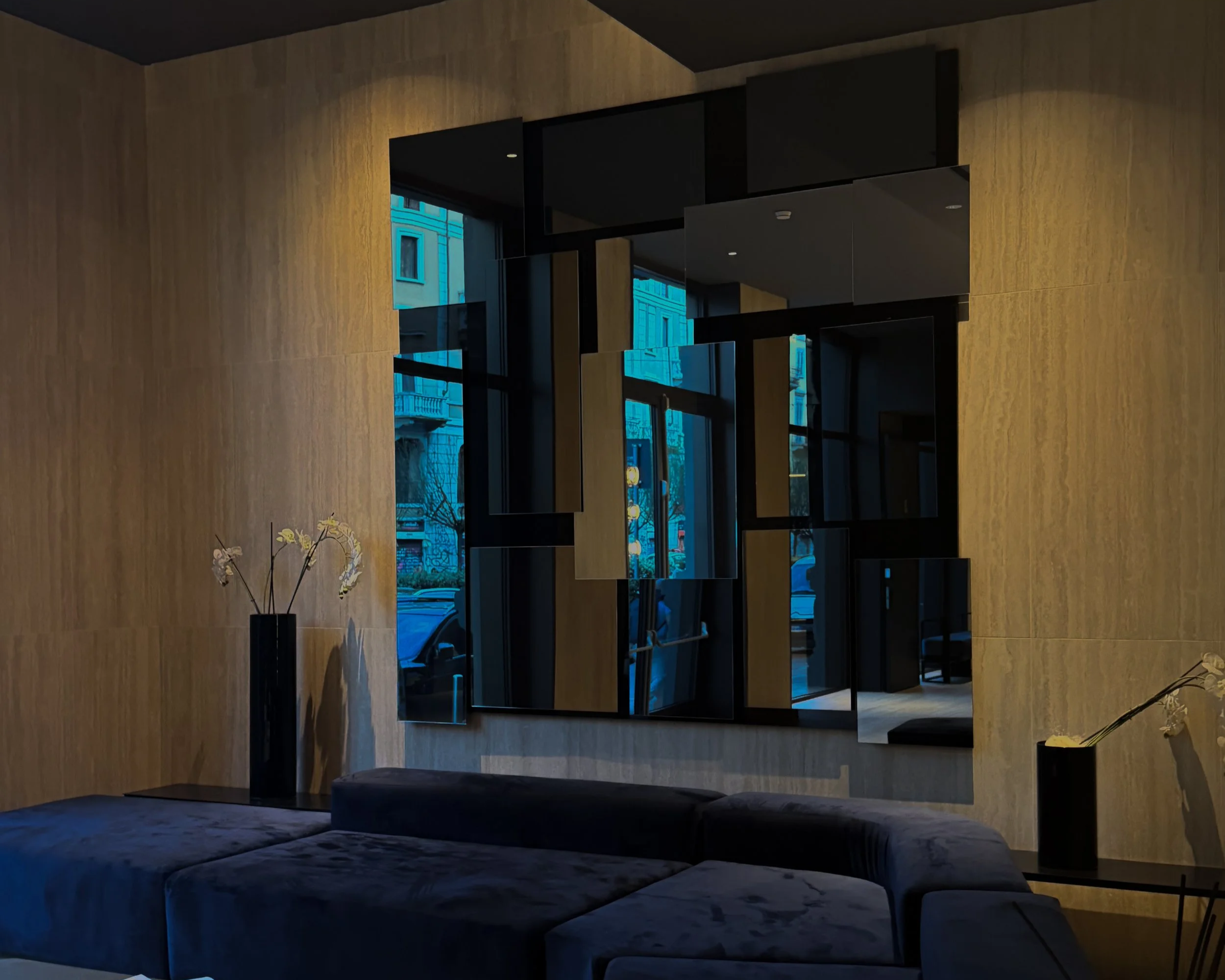Interior lounge at Palazzo Loreto Hotel in Milan with mirrored wall panels, dark seating, and warm lighting.