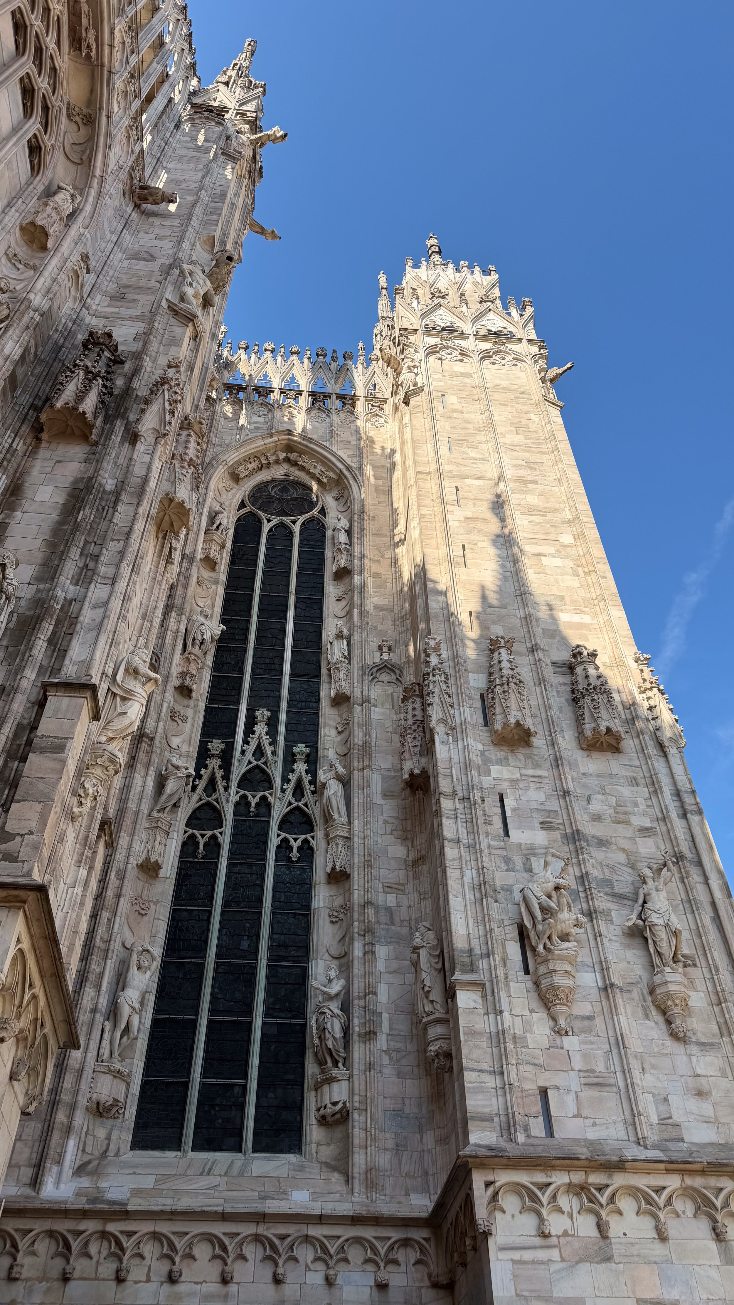 Milan Cathedral architectural detail with Gothic marble facade and blue sky.
