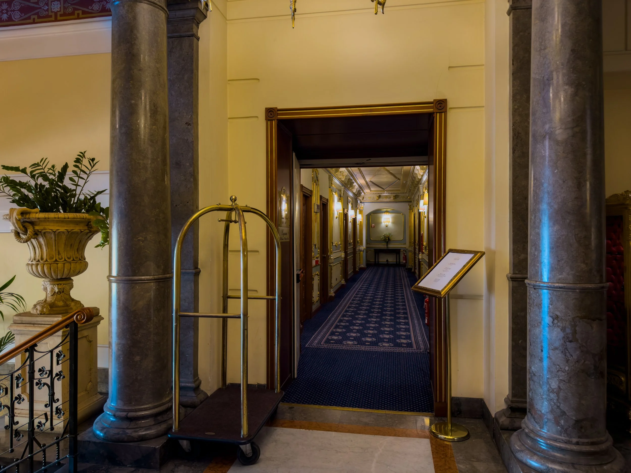 Marble columns, brass luggage trolley and ornate corridor inside Grand Hotel Wagner in Palermo.