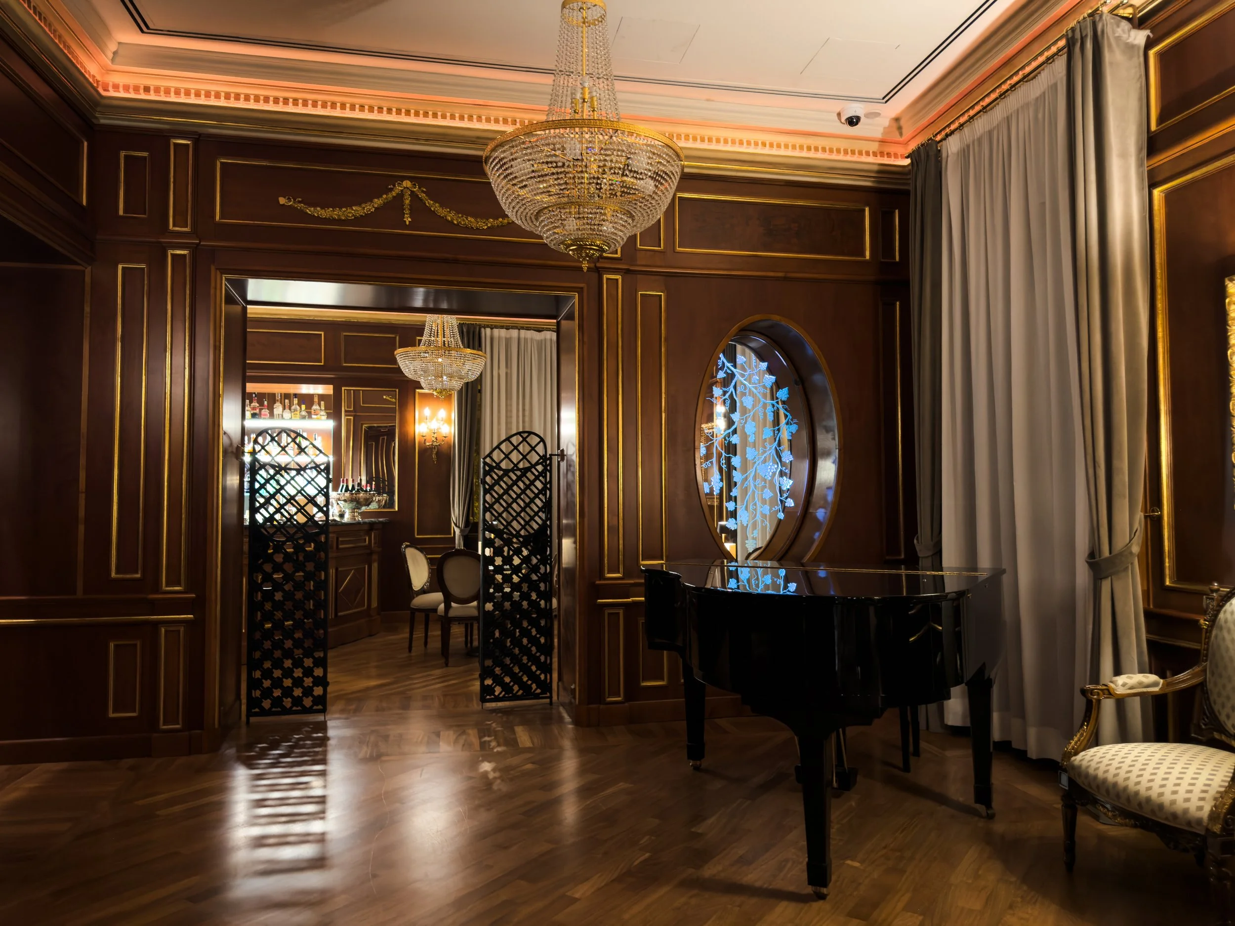 American Bar at Grand Hotel Wagner in Palermo with dark wood panelling, crystal chandeliers and a black grand piano.