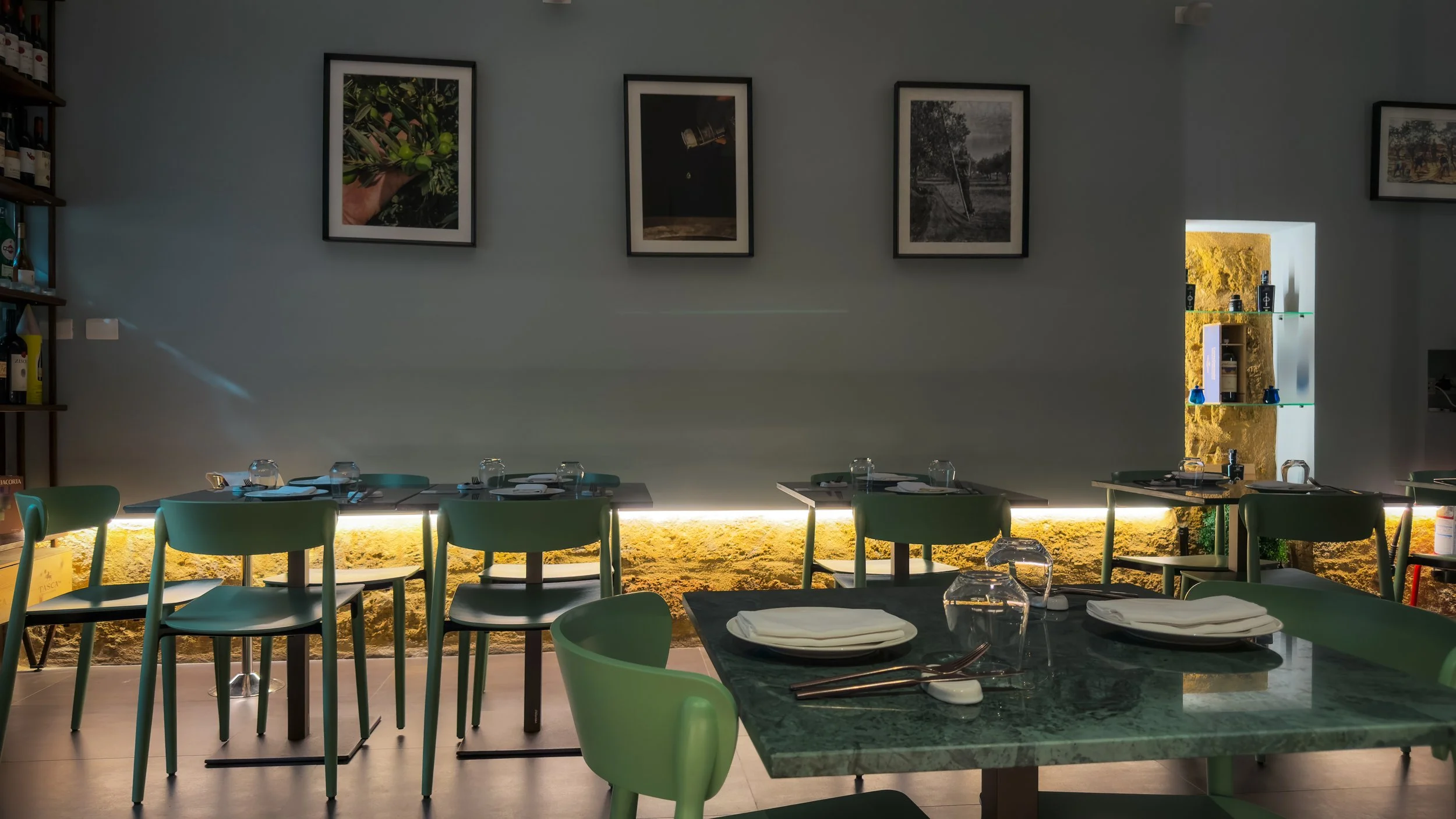 Dining room at Rimessa Dragotto in Palermo with green stone tables, green chairs and framed photographs on pale grey walls.