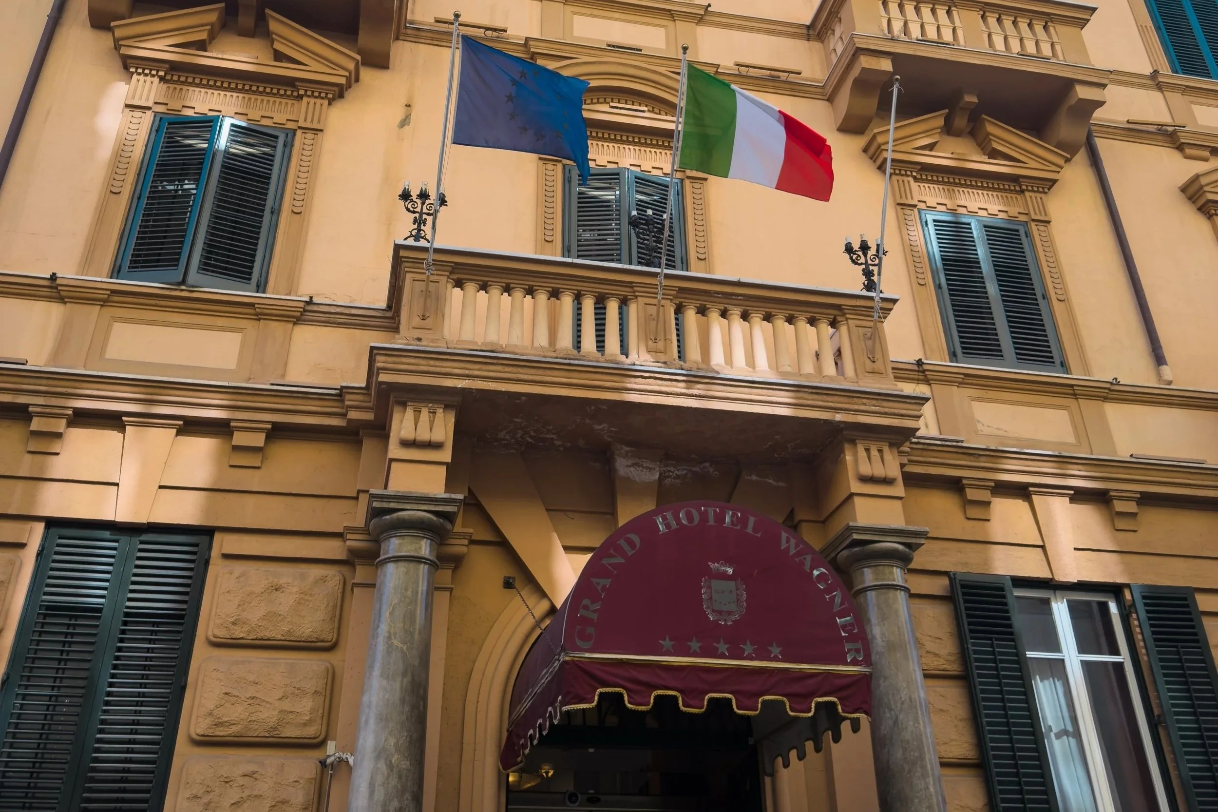Exterior façade and entrance of Grand Hotel Wagner in Palermo with Italian and European Union flags above the doorway.