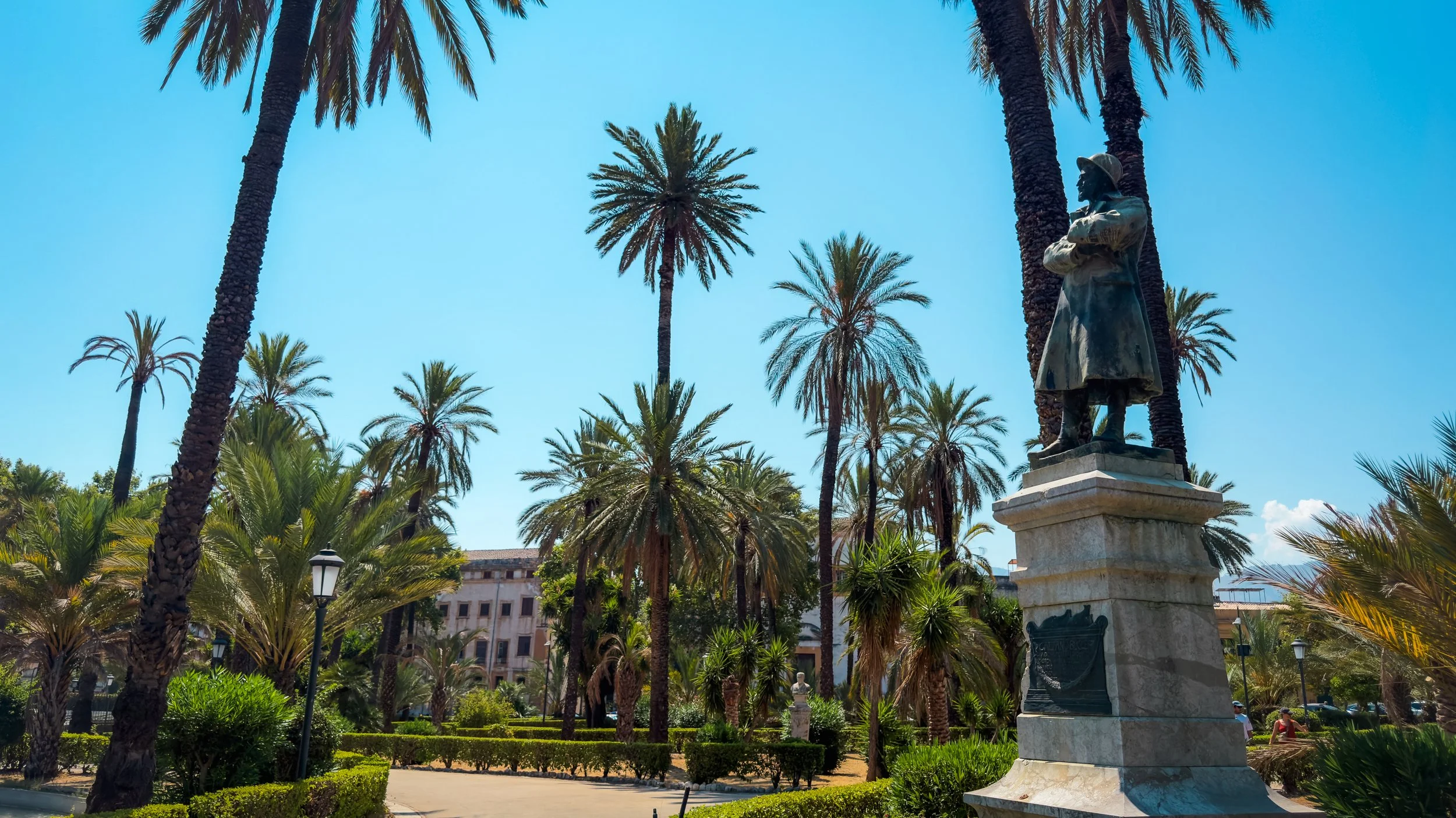 Bronze monument to Gaetano Bucceri surrounded by palm trees and gardens at Villa Bonanno in Palermo.