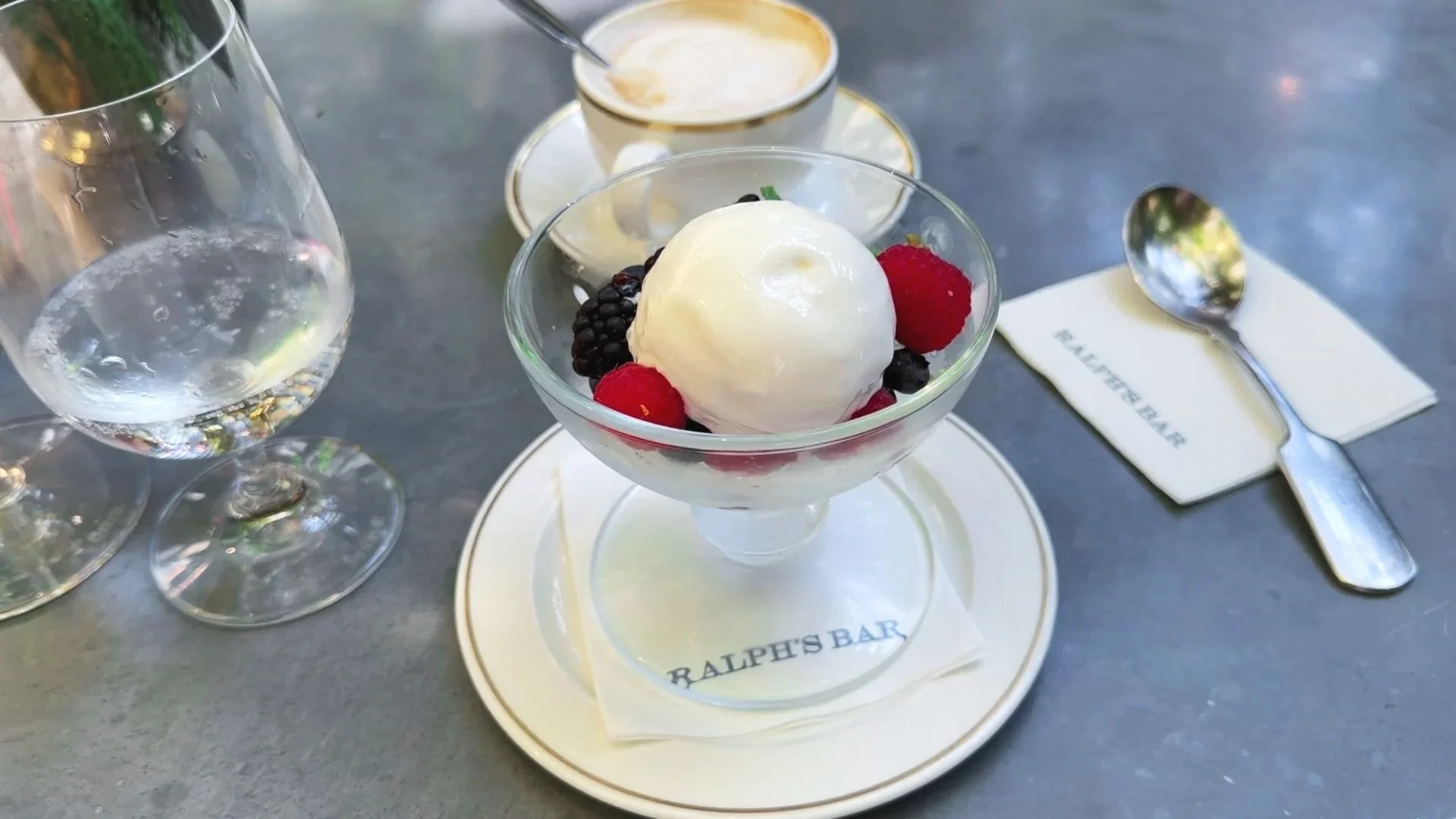 Vanilla gelato with raspberries and blackberries served in a glass dish at Ralph’s Bar Milano, with coffee and branded tableware.