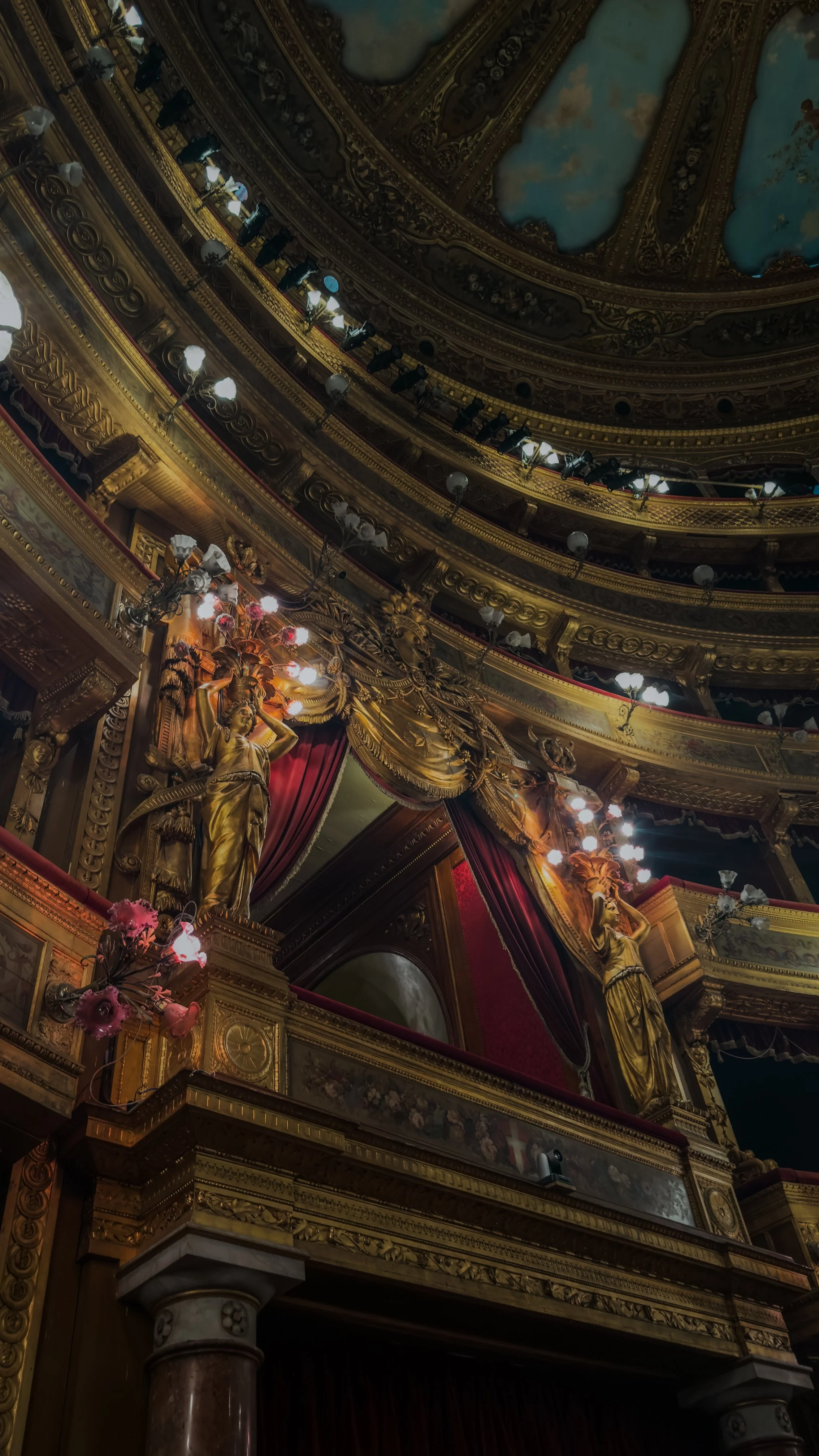 Gilded theatre box with red velvet curtains and sculpted figures inside Teatro Massimo in Palermo.