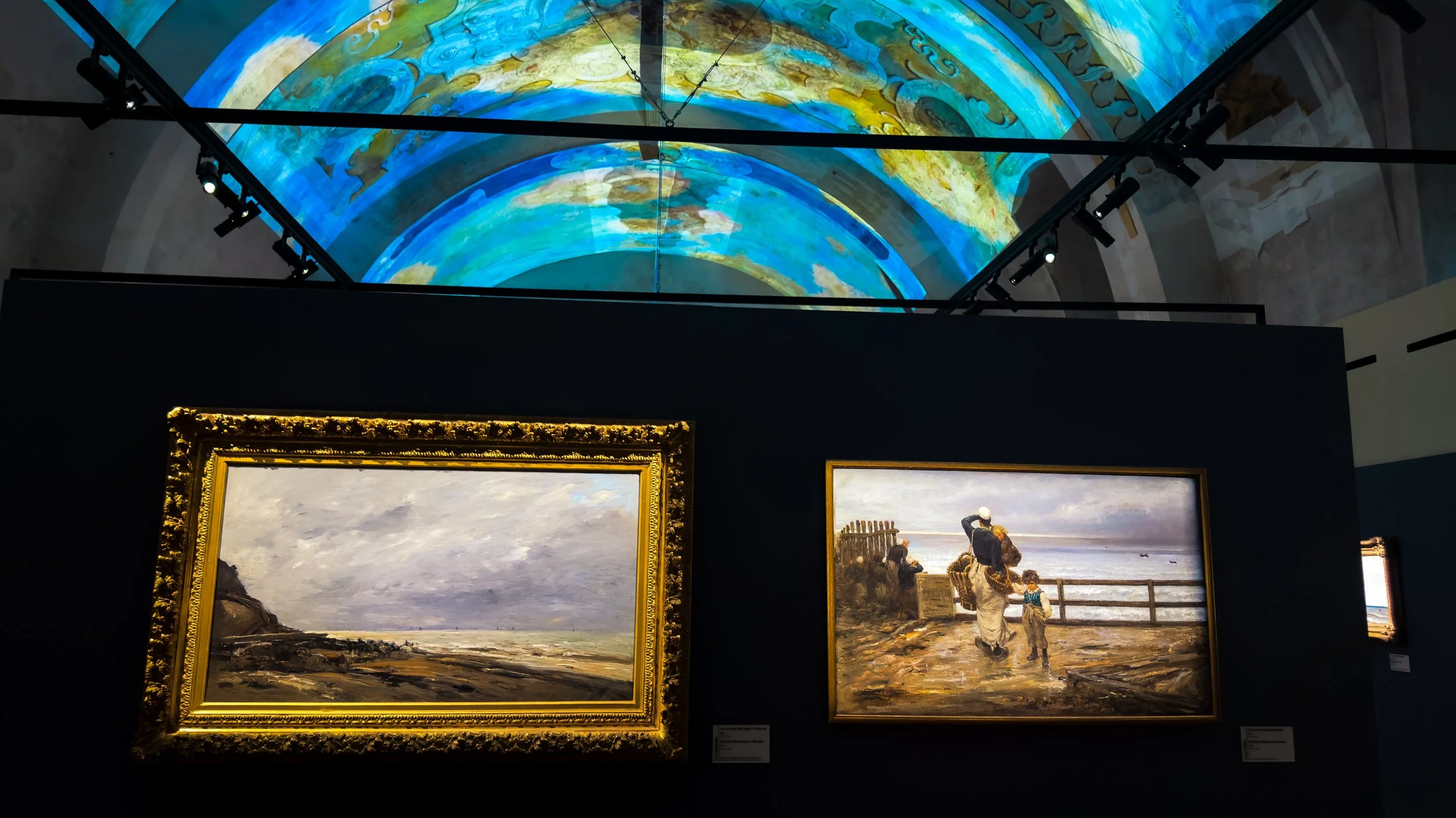 Framed Impressionist paintings displayed beneath an illuminated painted vaulted ceiling at Palazzo dei Normanni in Palermo.