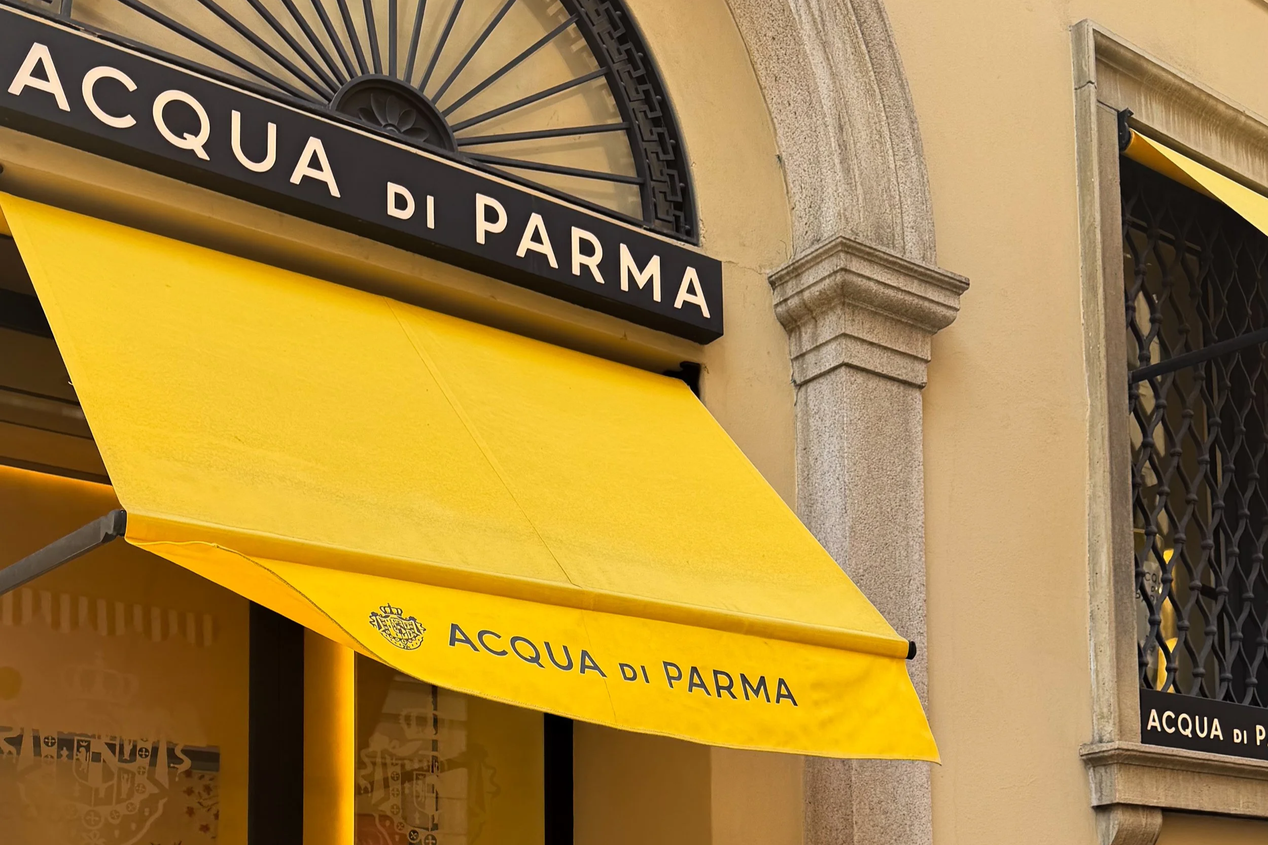 Acqua di Parma storefront in Milan with a yellow awning and historic building facade.