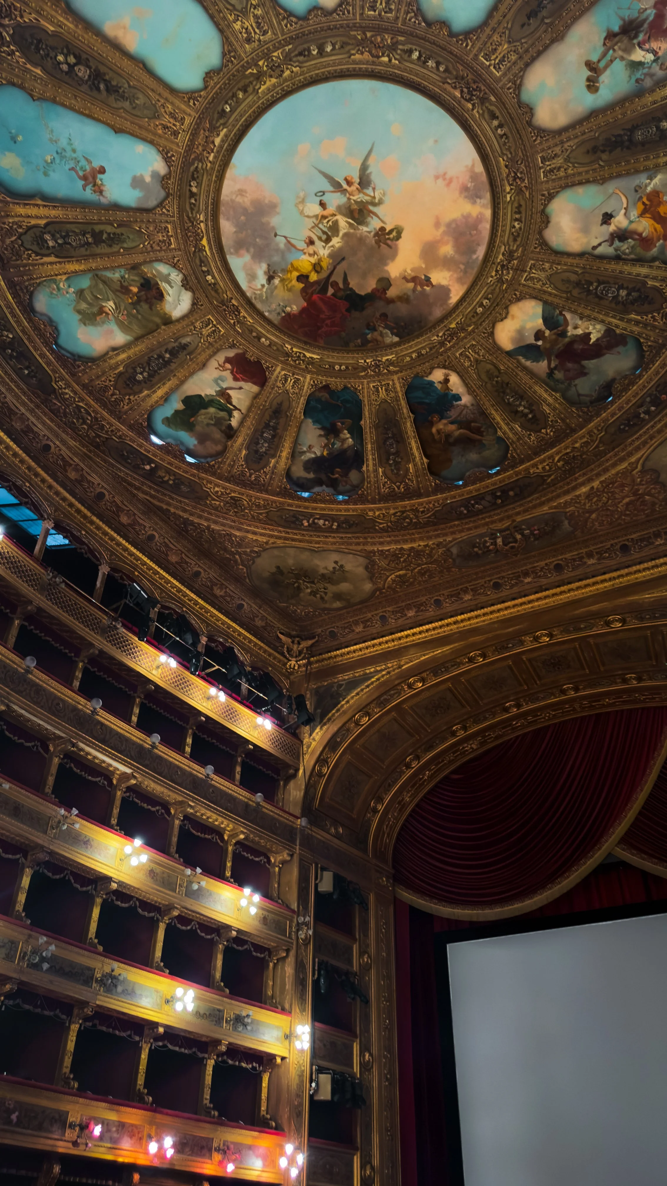 Interior of Teatro Massimo in Palermo showing the painted ceiling, gilded balconies and red stage curtain.