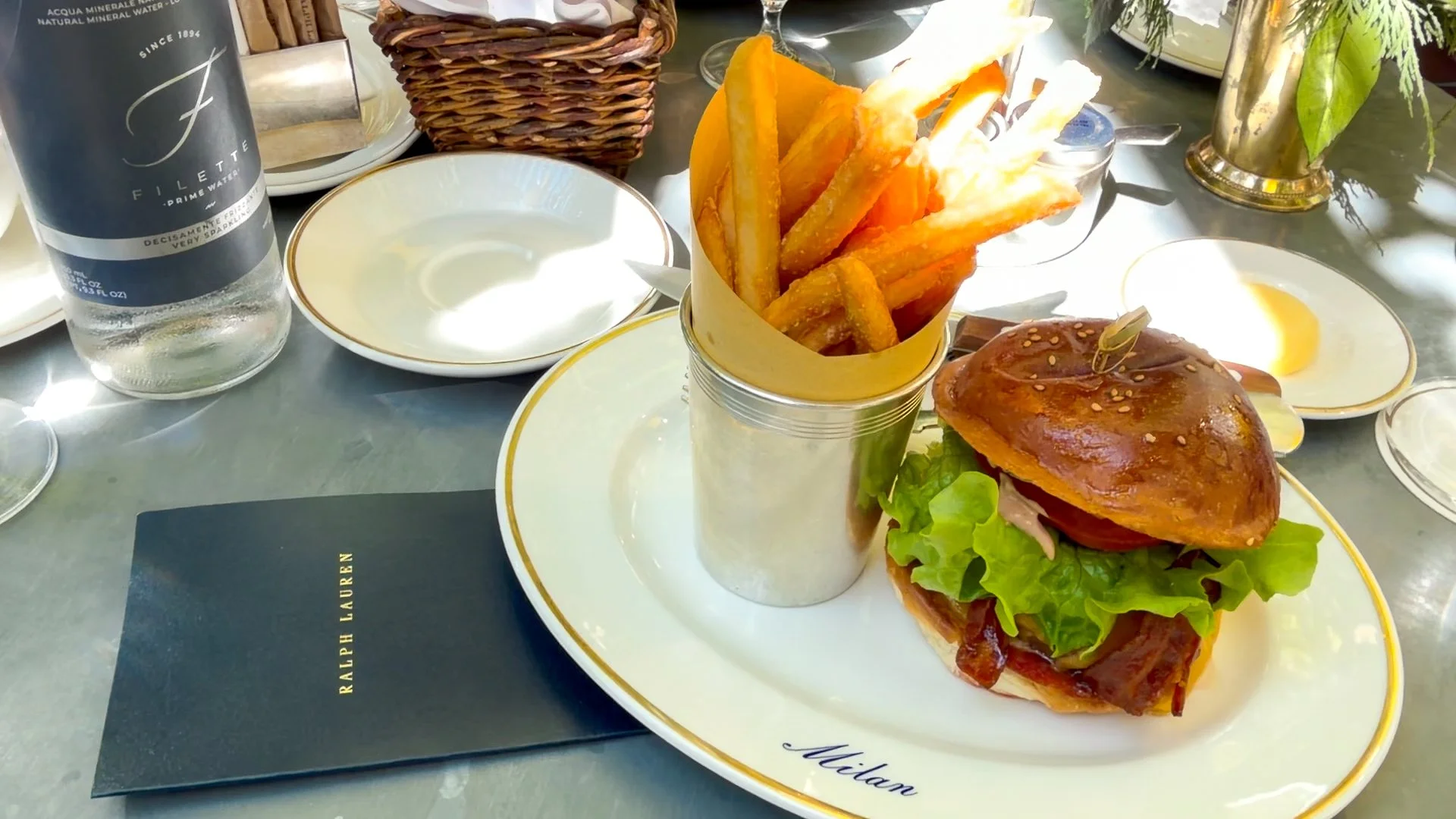 Close view of the Ralph’s Bar Milano burger with bacon, lettuce, tomato and thick-cut fries on branded tableware.