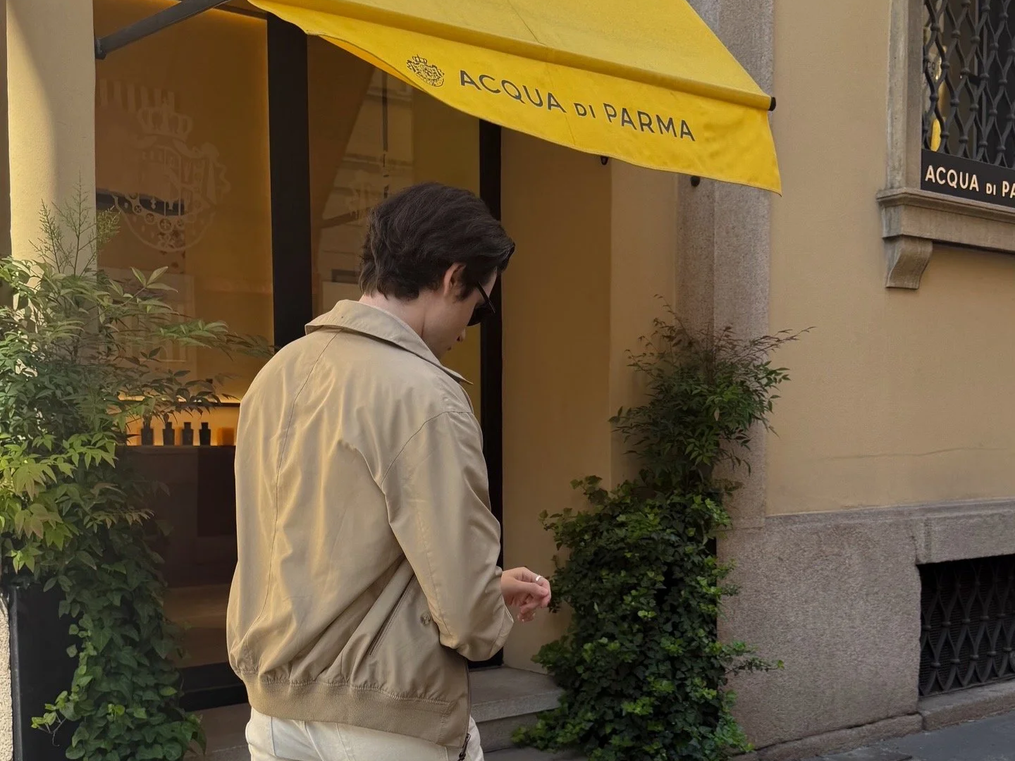 Man standing outside the Acqua di Parma store in Milan beneath the yellow storefront awning.