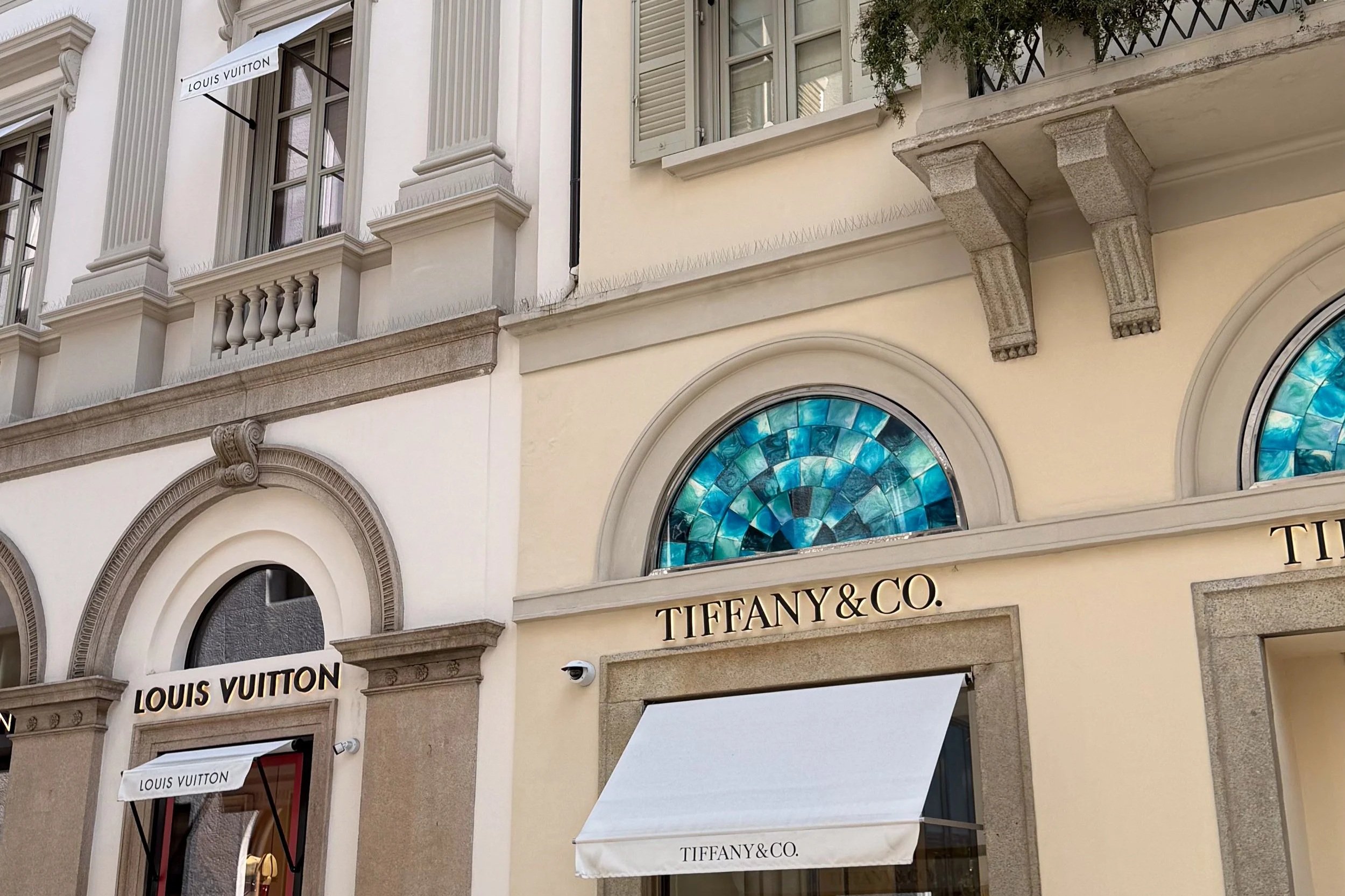 Luxury storefronts on Via Montenapoleone in Milan, including Louis Vuitton and Tiffany & Co.