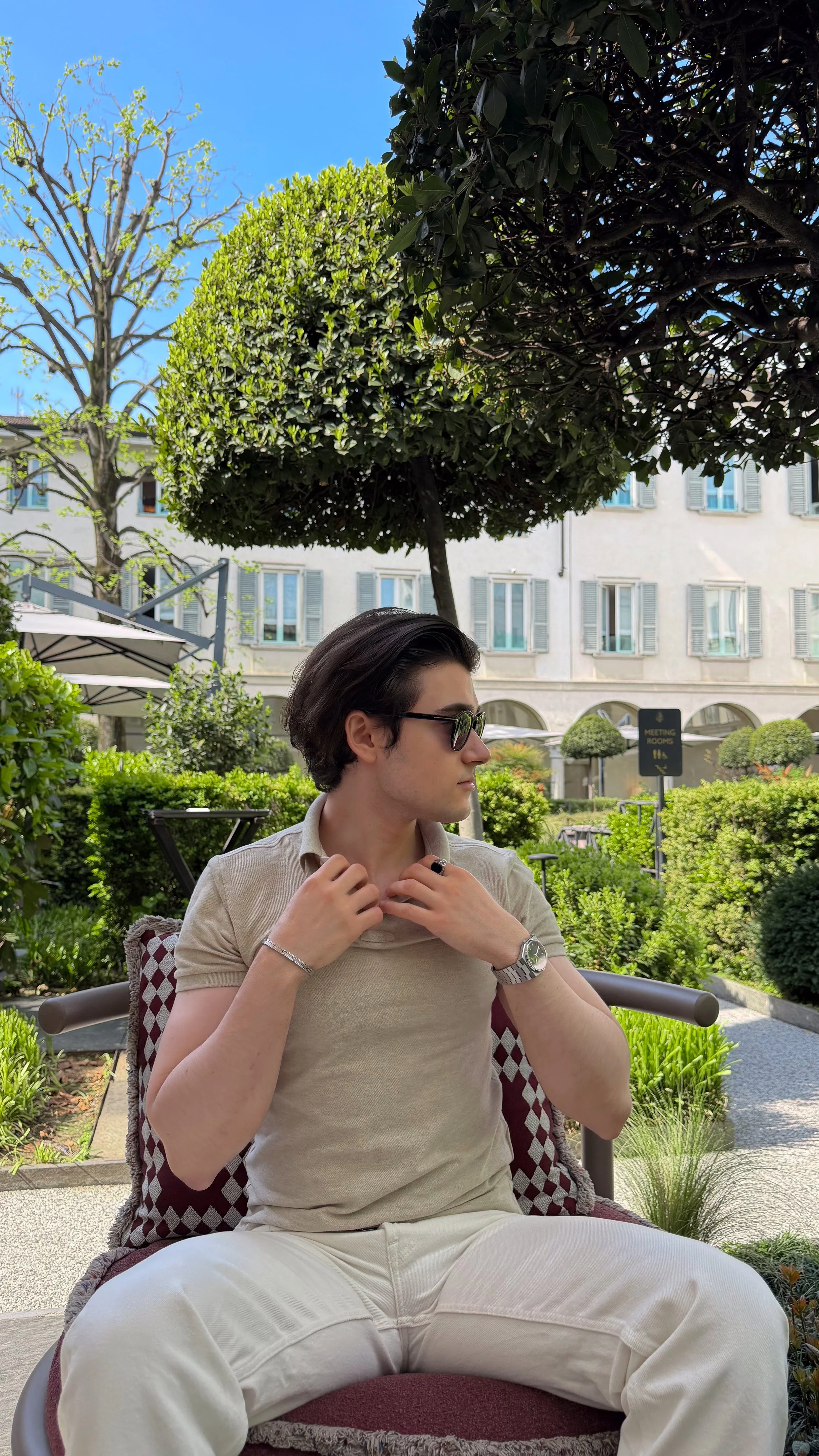 Guest seated in the landscaped courtyard at Stilla Garden, Four Seasons Hotel Milano, wearing a neutral-toned outfit and sunglasses.