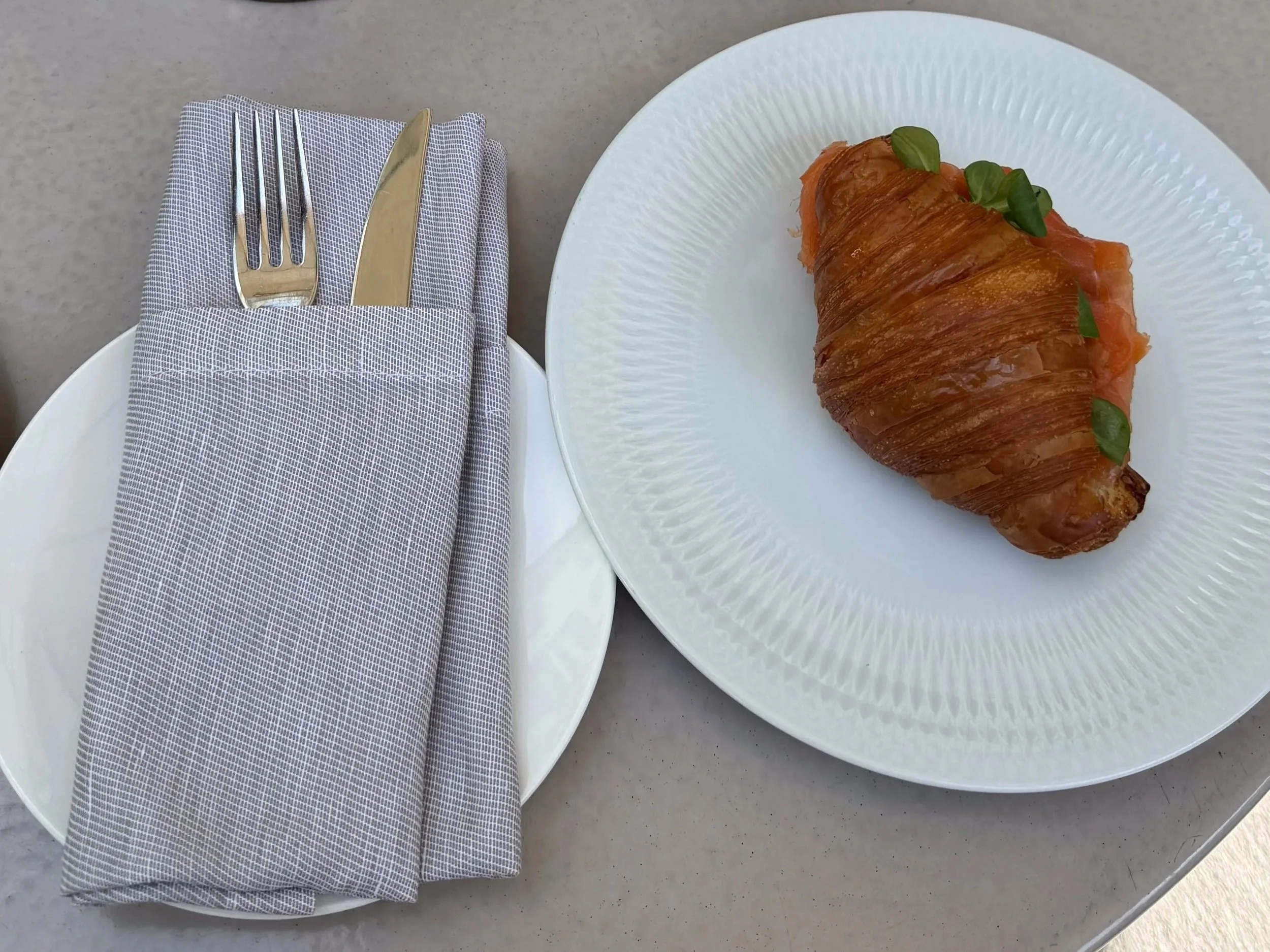 Smoked salmon croissant served for breakfast at Stilla Garden, Four Seasons Hotel Milano, beside a neatly folded napkin and cutlery.