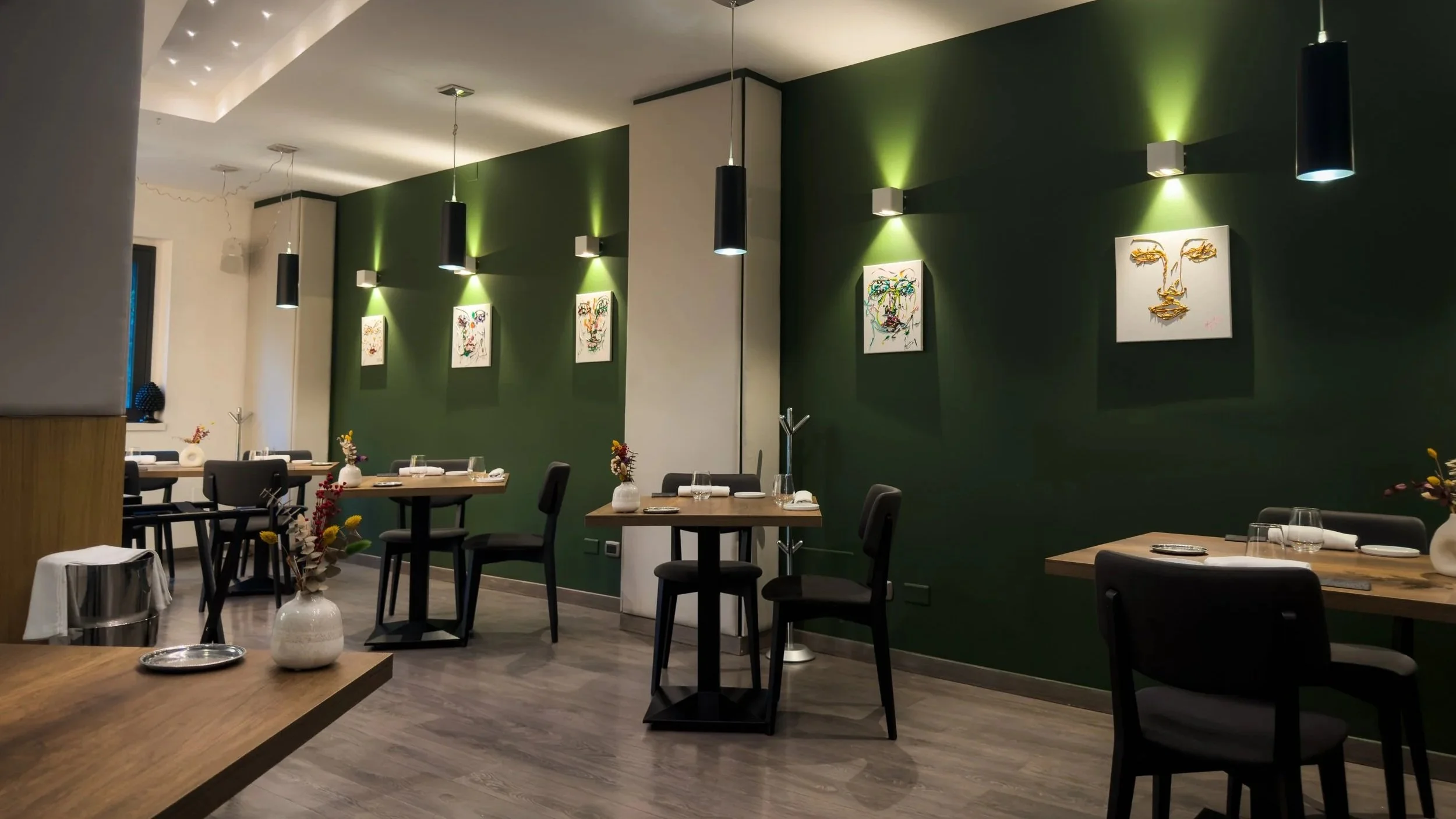 Dining room at ALI3I in Palermo with dark green walls, wooden tables, black chairs and framed artwork.