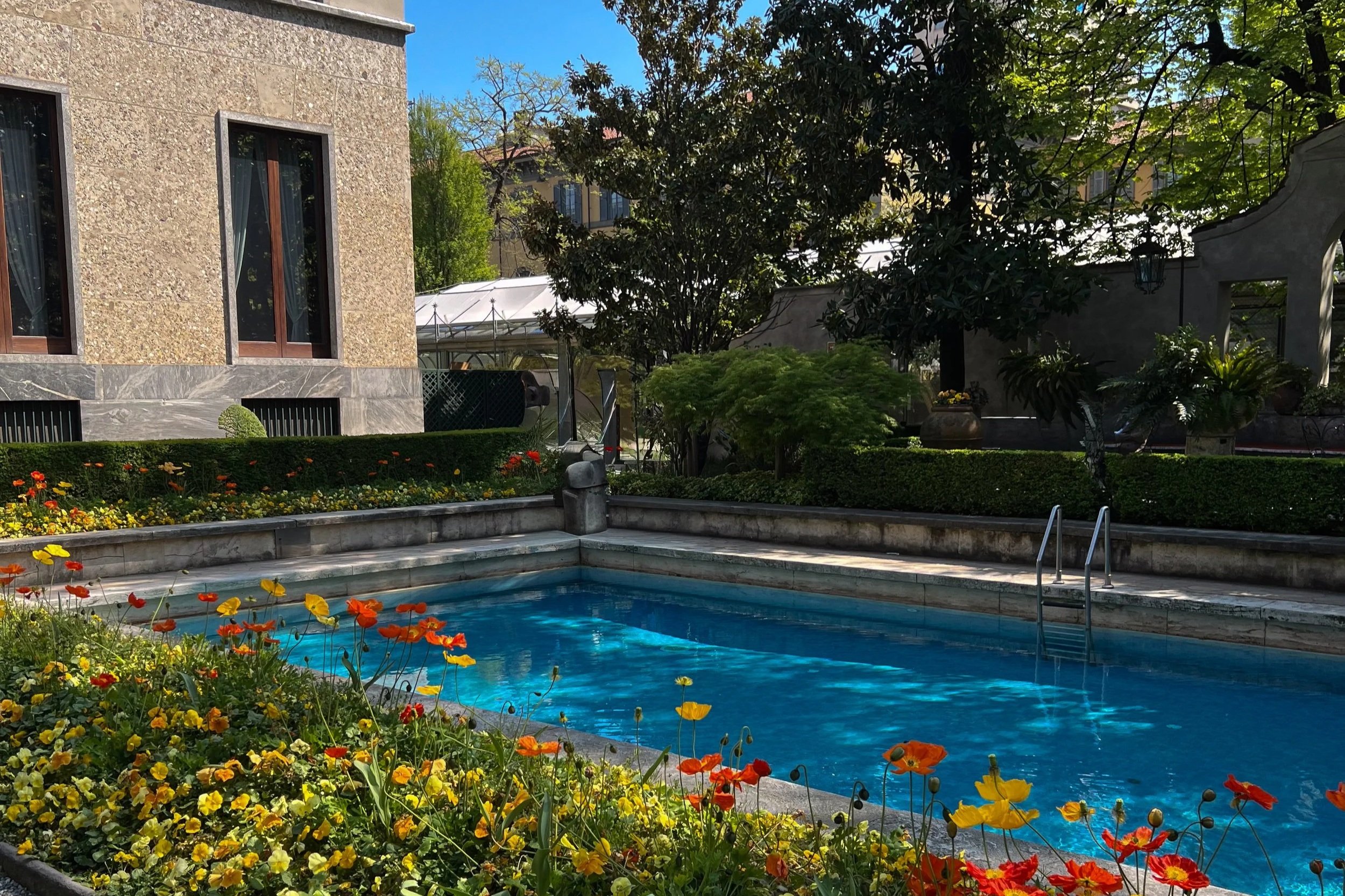 Garden and swimming pool at Villa Necchi Campiglio in Milan with flowers, trees, and historic architecture.