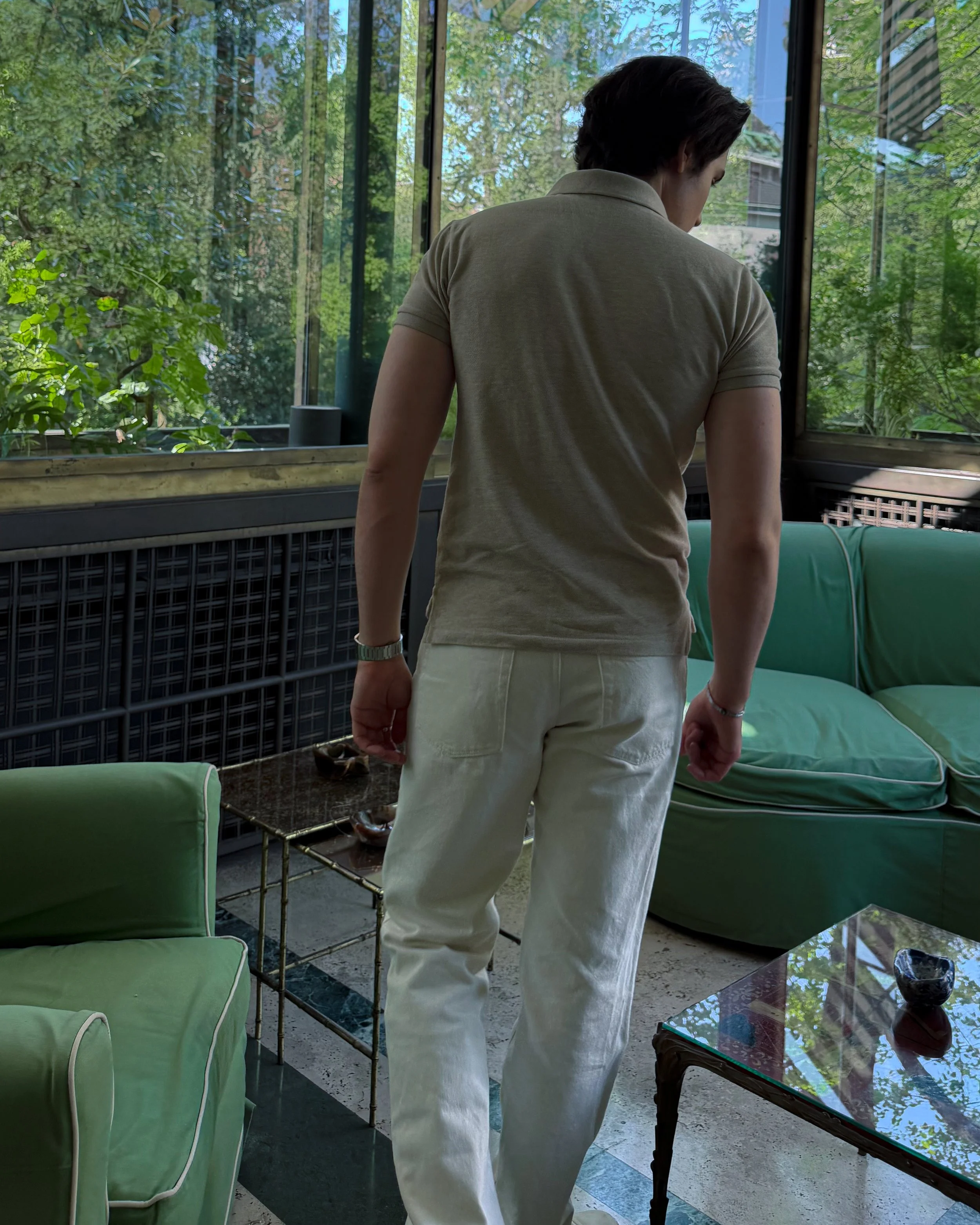Interior room at Villa Necchi Campiglio in Milan with green seating, glass windows, and garden views.