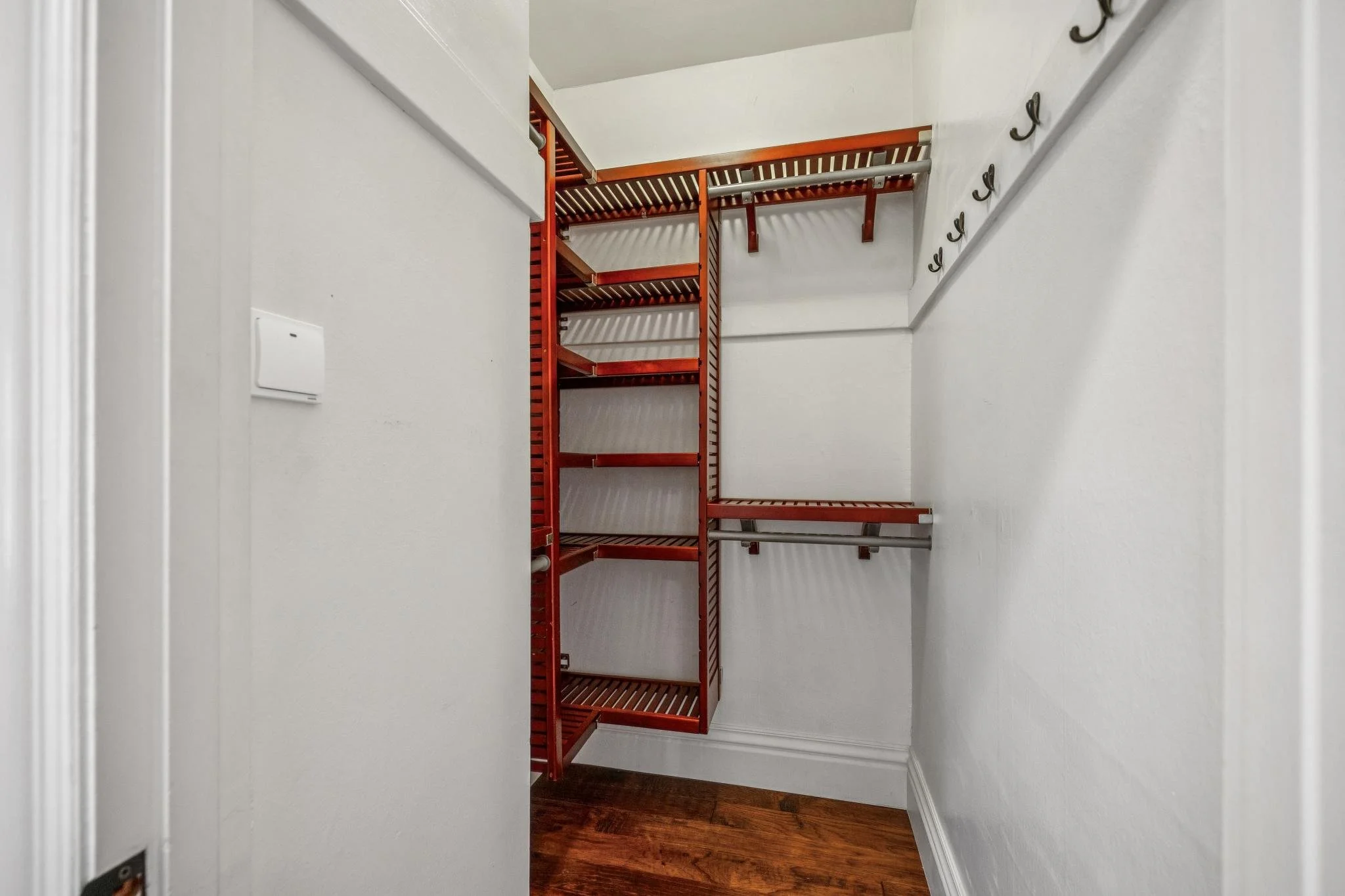 Empty walk-in closet with white walls, dark hardwood flooring, and red metal shelves.