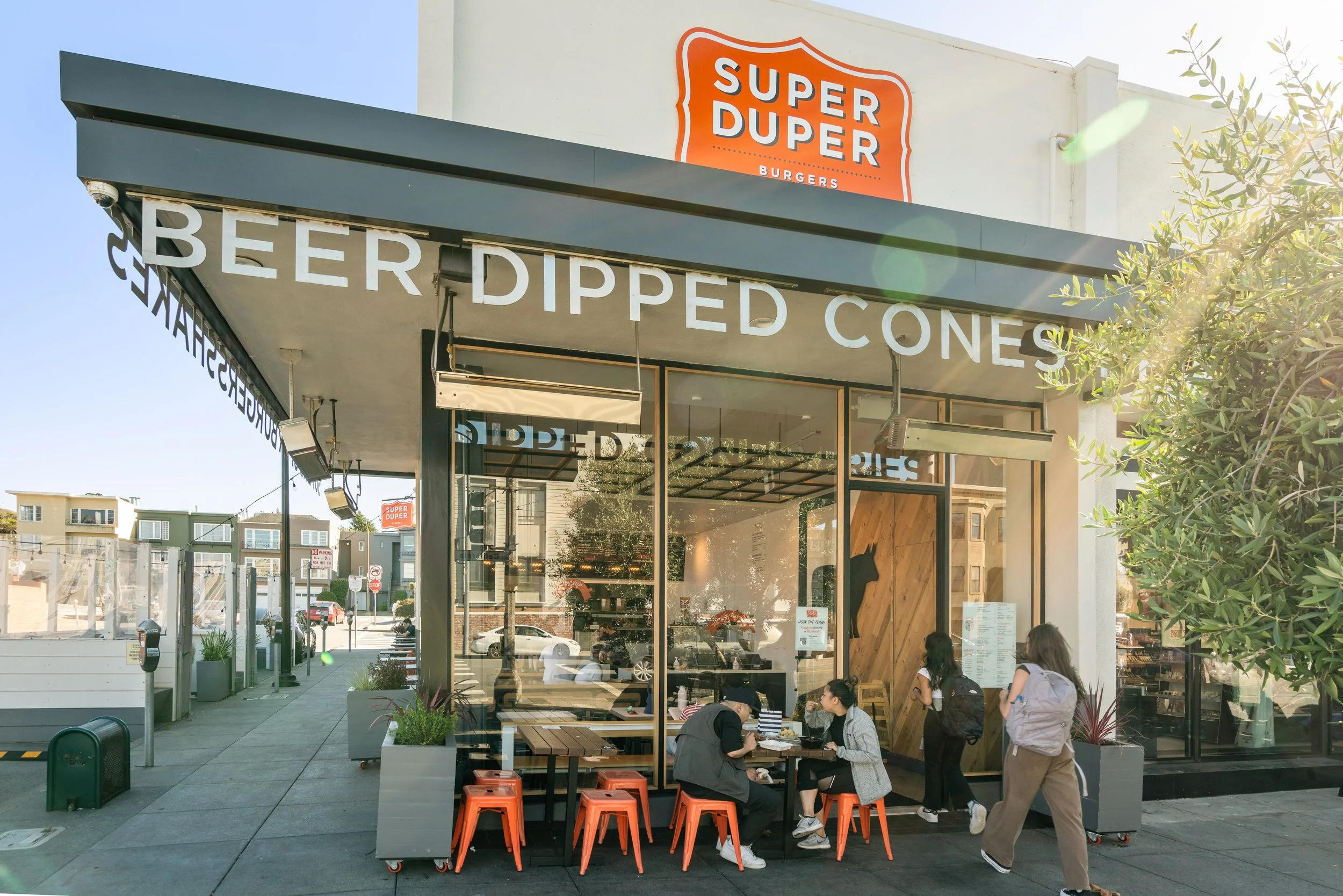 Outside view of a burger restaurant named Super Duper Burgers with people sitting outside and waiting in line