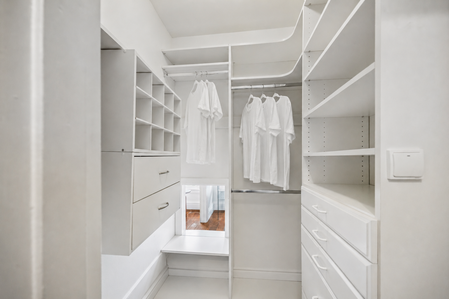 Empty white walk-in closet with hanging clothes, shelves, and drawers