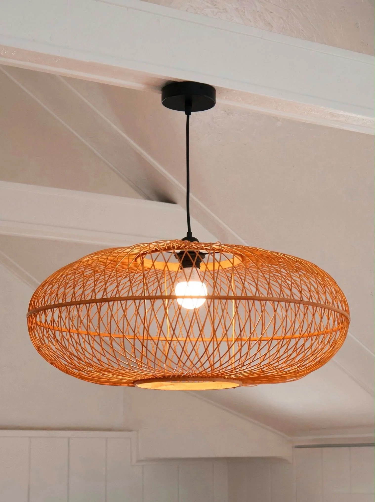 Orange woven pendant light fixture hanging from the ceiling with a black ceiling mount and cord, in a room with white ceiling and walls.