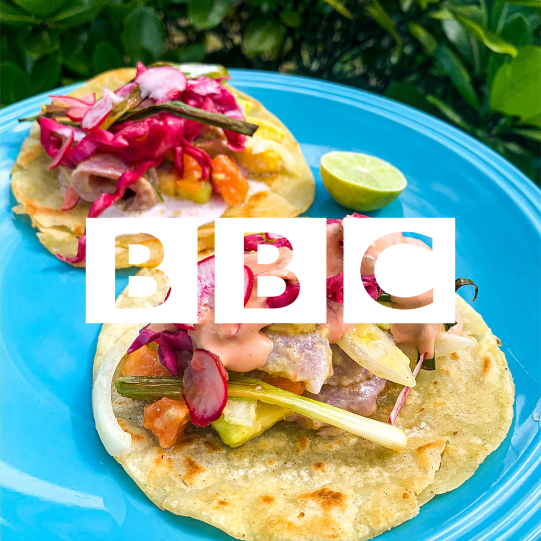 Tacos avec de la viande, des légumes, de la sauce et un citron vert coupé, sur une assiette bleue.