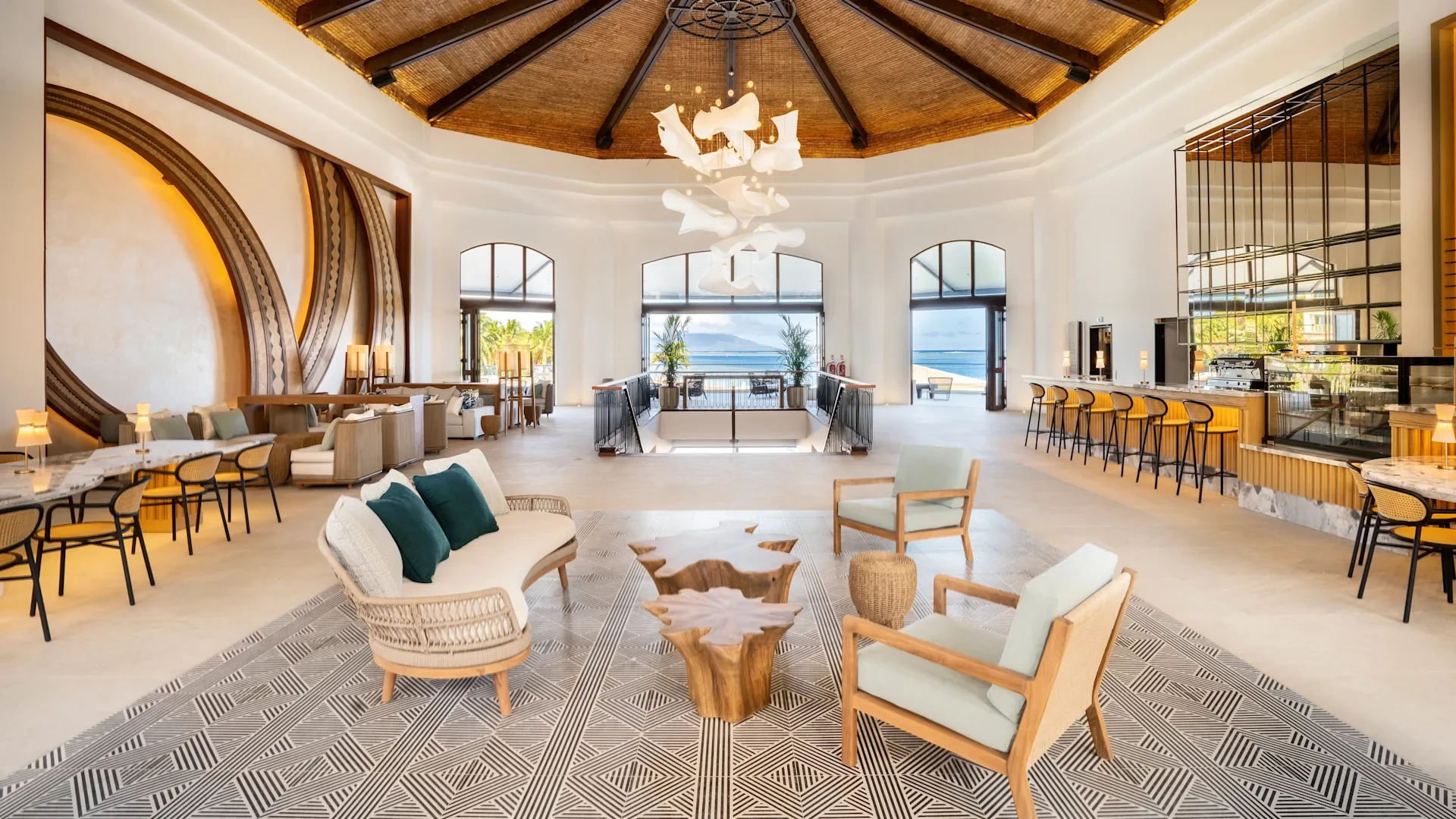 Salon intérieur avec des meubles en rotin, un bar avec des tabourets en bois, fenêtres avec vue sur la mer et décoration moderne, ambiance lumineuse et chaleureuse.