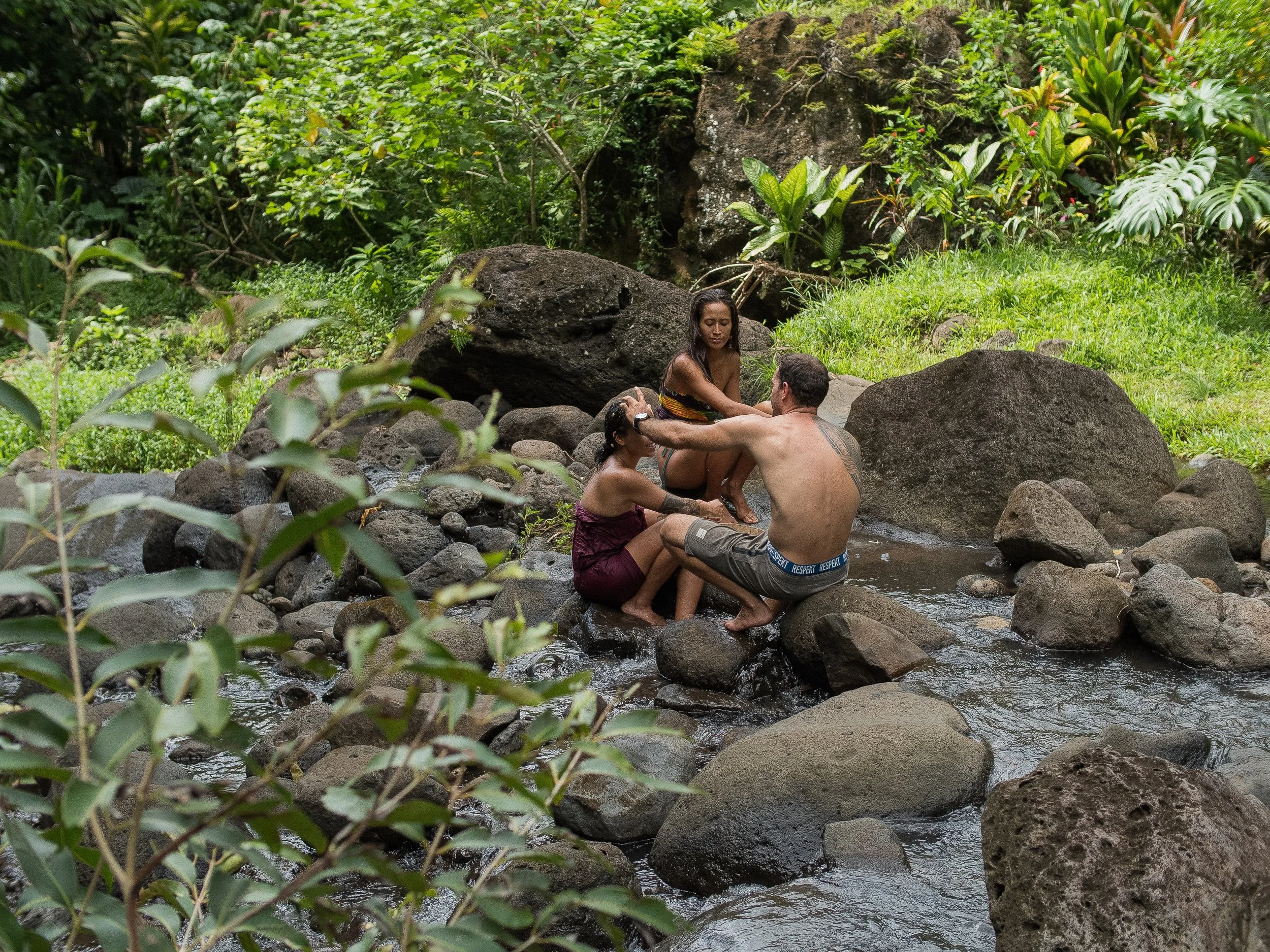 Trois personnes dans une rivière entourée de verdure, en train de se baigner et de profiter du paysage naturel.