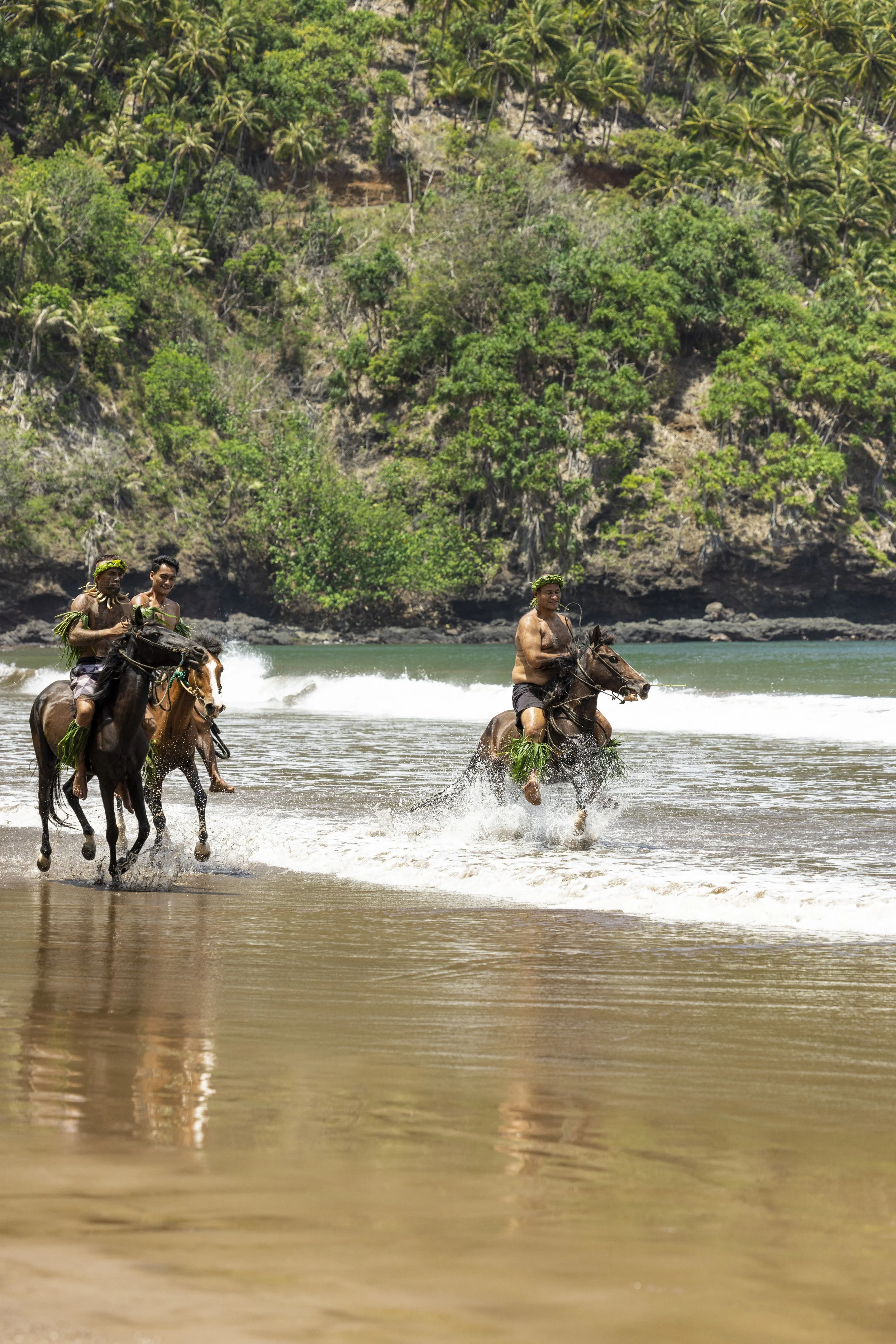Trois personnes montent à cheval dans la mer avec une végétation luxuriante en arrière-plan.