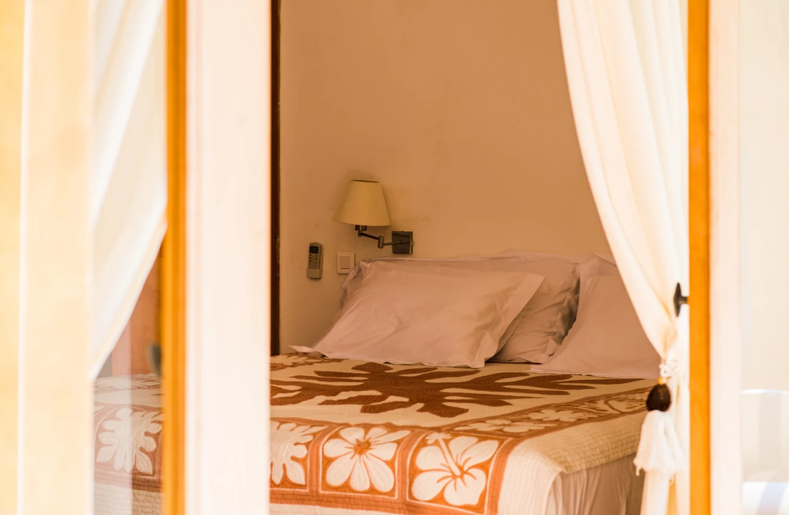 Vue d'un lit dans une chambre d'hôtel avec des rideaux blancs, une lampe de veilleuse, et une télécommande accrochée au mur.