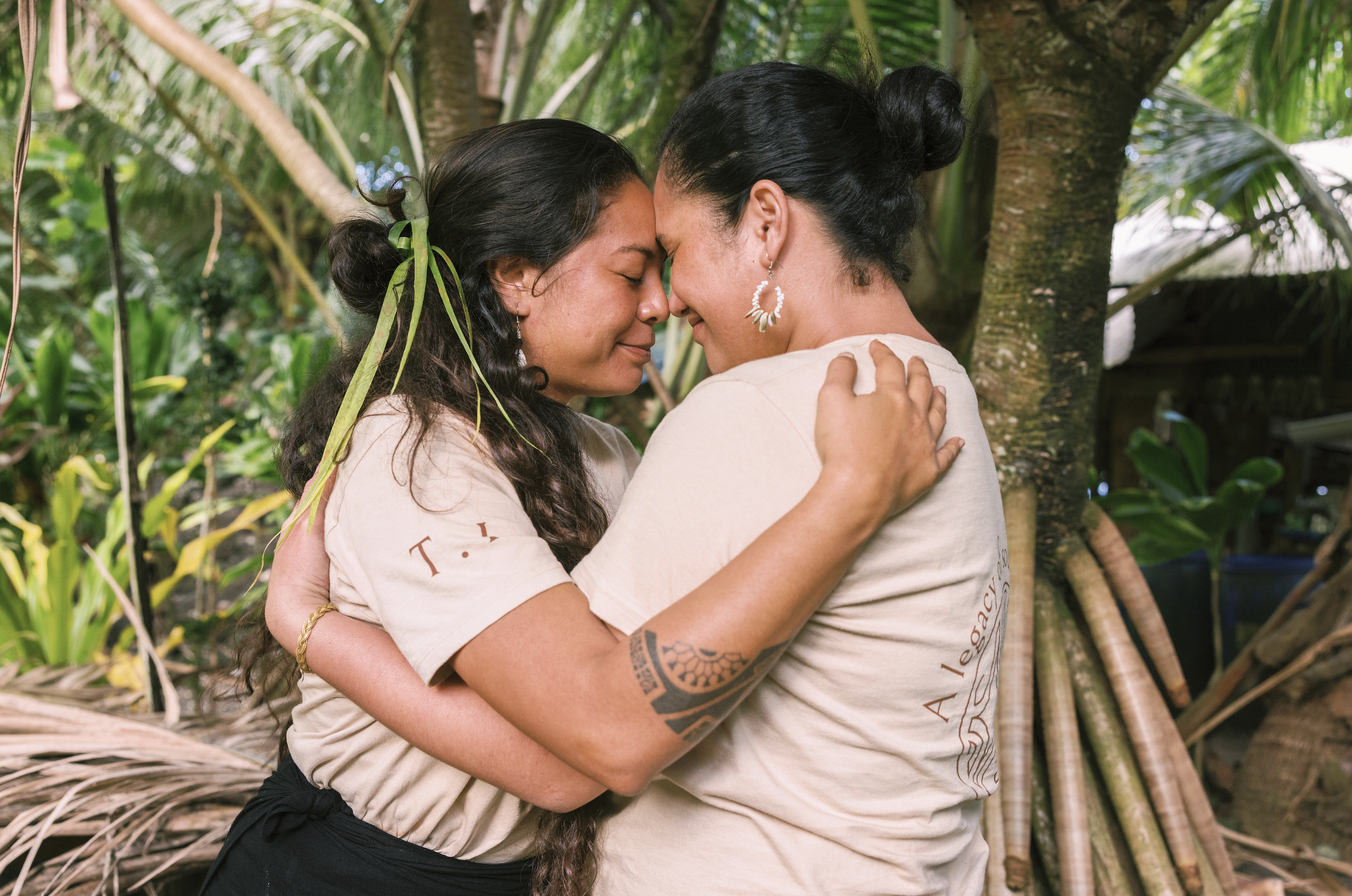 Deux femmes s'embrassent tendrement au milieu d'un environnement luxuriant avec des arbres et des plantes vertes.