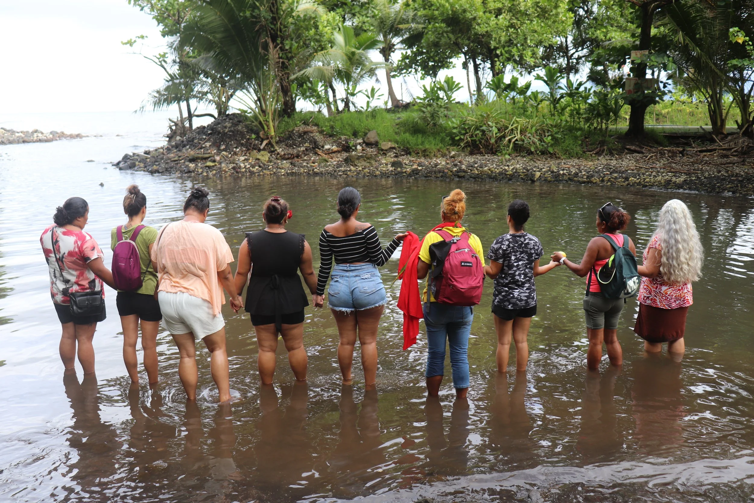 Groupe de personnes debout dans un cours d'eau, avec des arbres et de la végétation tropicale en arrière-plan.