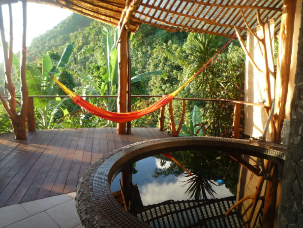 Terrasse en bois avec un hamac rouge, vue sur la forêt tropicale dense, piscine ou jacuzzi à proximité, ambiance relaxante