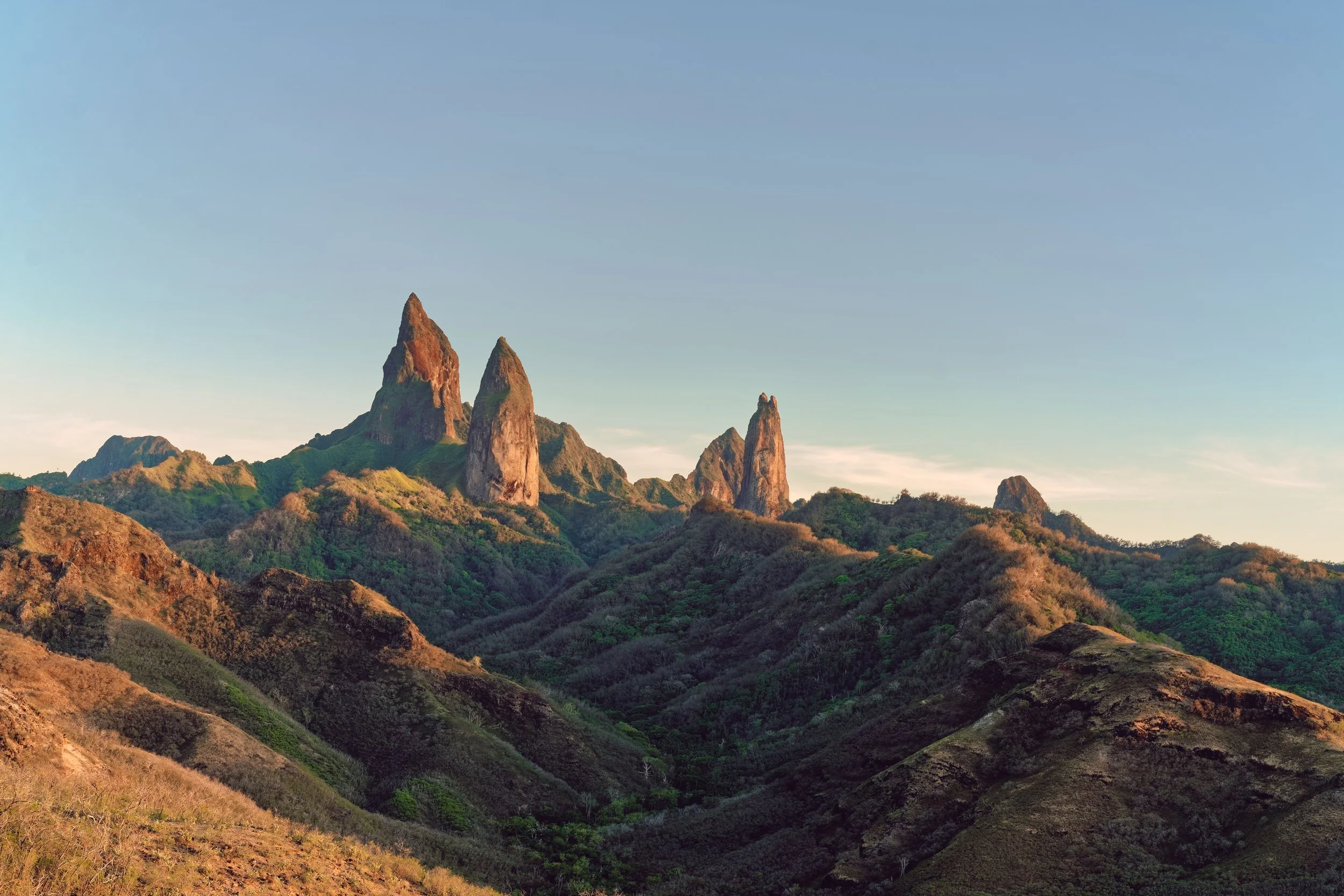 Montagnes avec trois pics rocheux pointus entourés de végétation verte, sous un ciel clair.