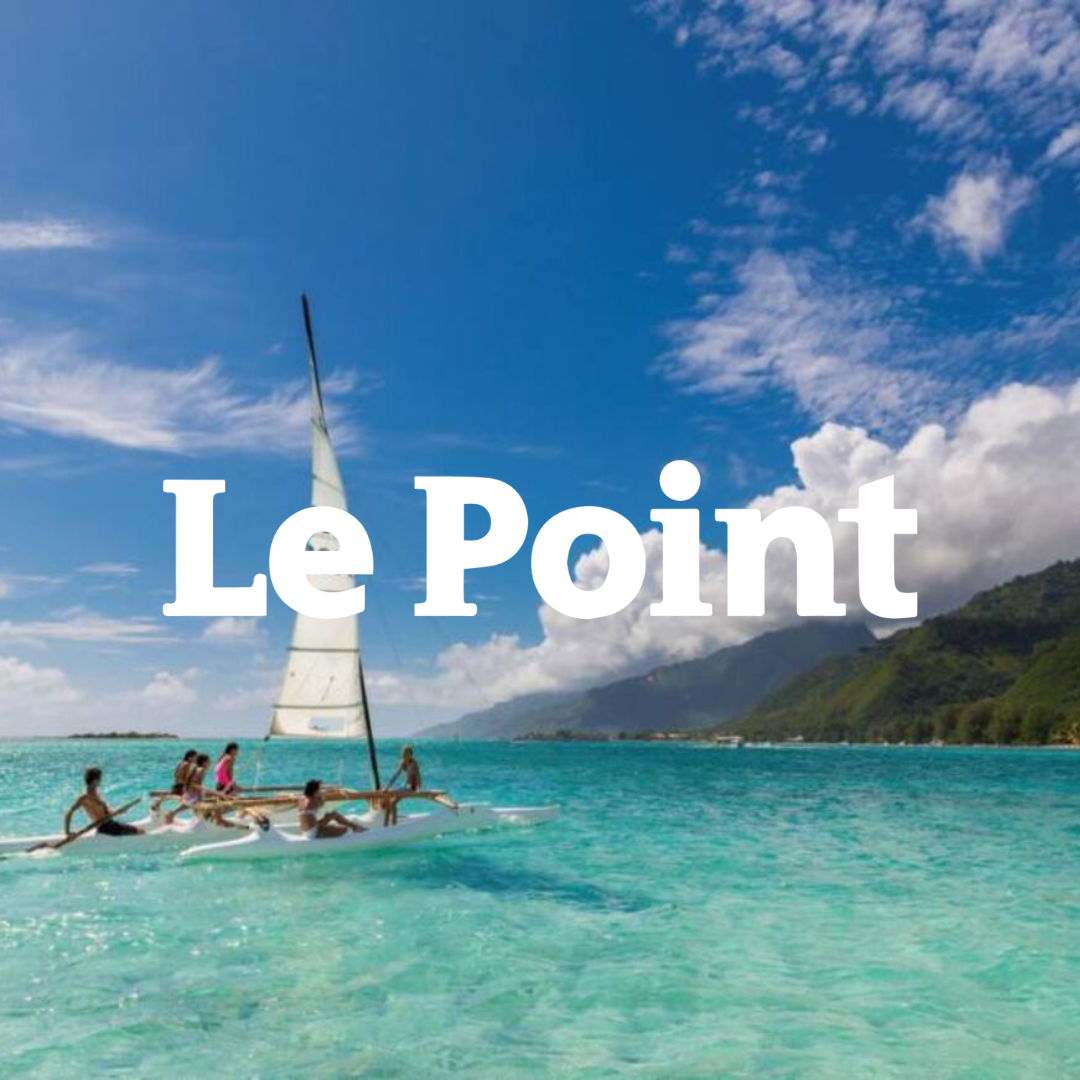 Un groupe de personnes naviguant en bateau à voile sur une mer turquoise avec des montagnes verdoyantes en arrière-plan sous un ciel bleu avec quelques nuages.