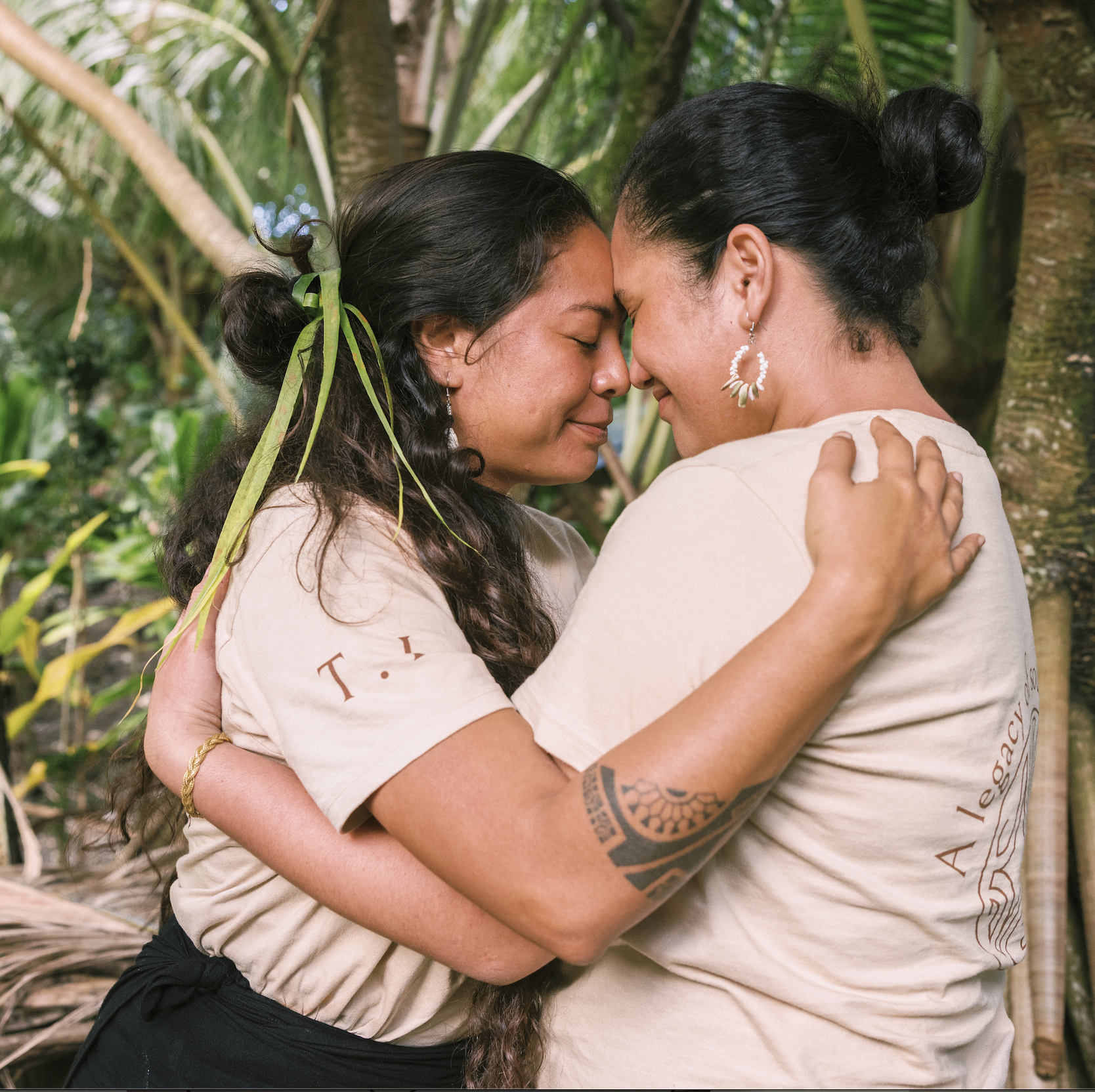 Deux femmes s'embrassent tendrement avec les fronts touchés, en pleine nature, entourées de végétation verte tropicale.