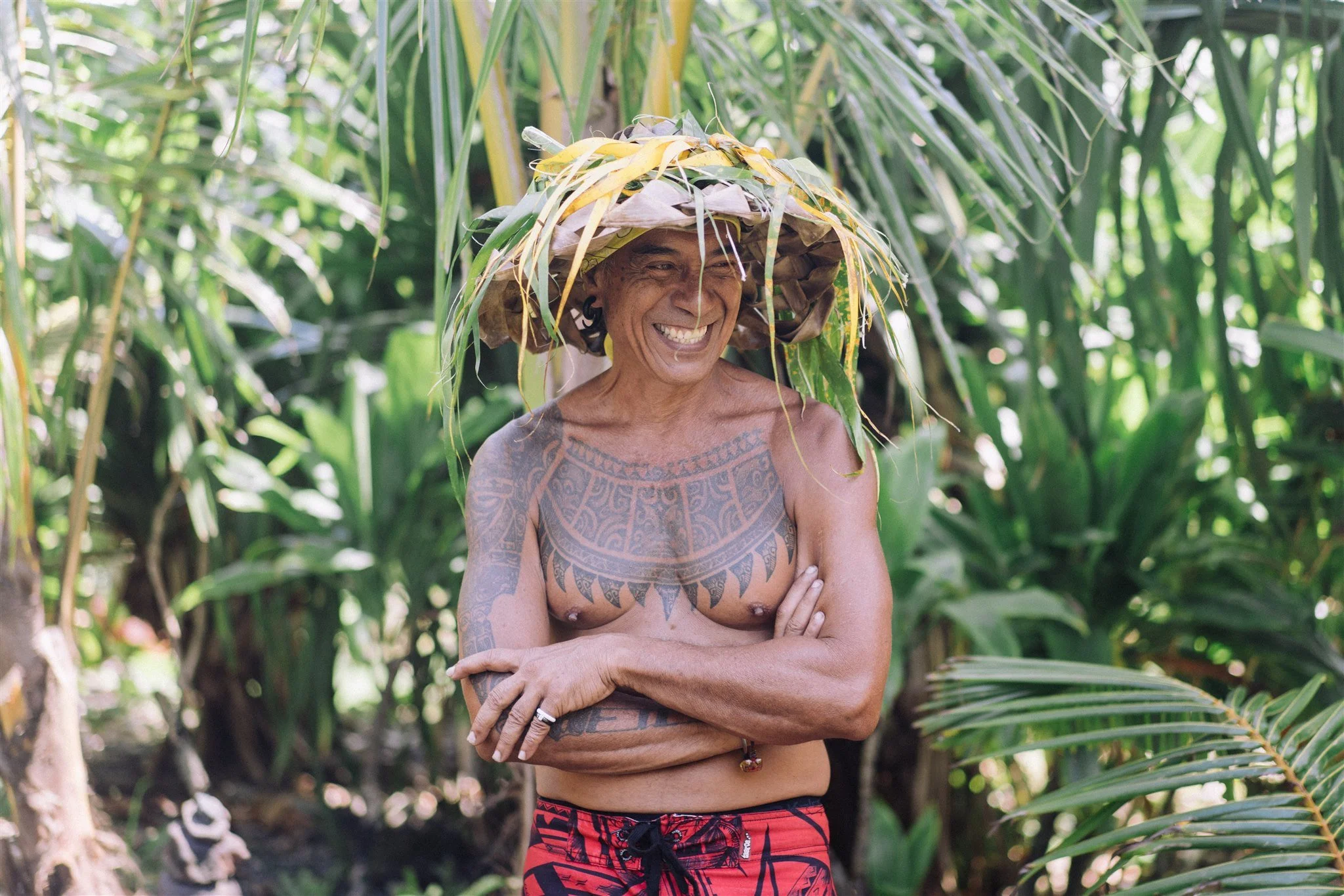 Un homme tatoué souriant portant un chapeau en feuilles dans une forêt tropicale