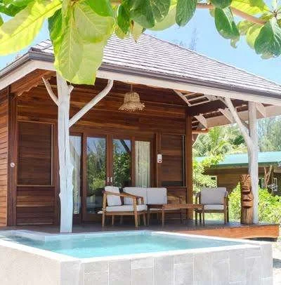 Petite maison en bois avec terrasse, mobilier d'extérieur, piscine, entourée de verdure tropicale.