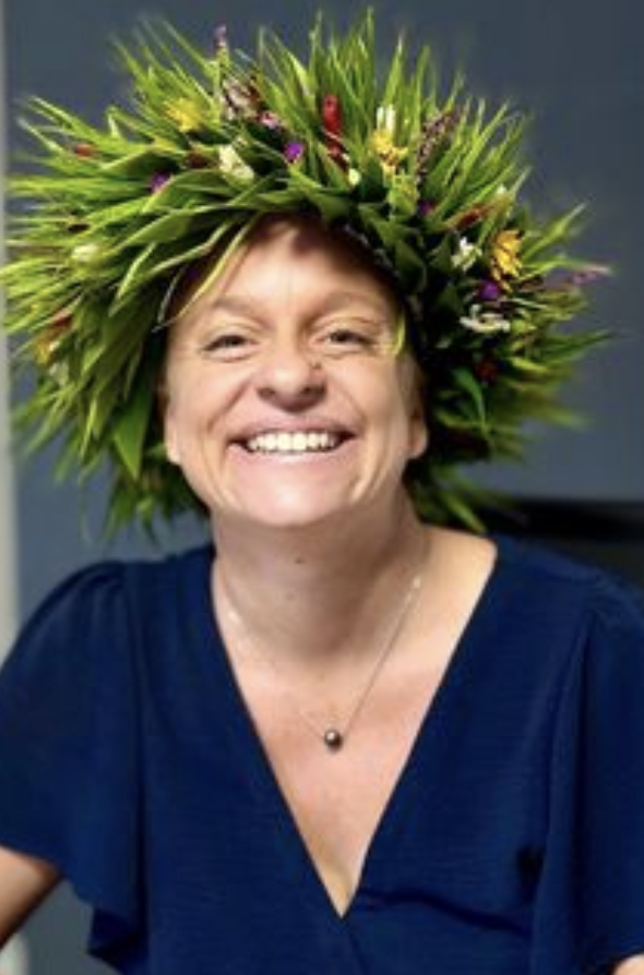 Femme souriante portant une couronne faite de fleurs et de longues feuilles vertes.