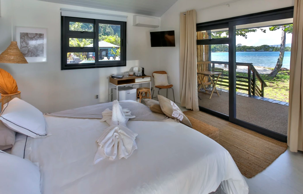 Chambre d'hôtel avec vue sur la mer, lit avec serviettes pliées en forme de cygne, balcon avec chaise et vue sur la plage et les arbres.