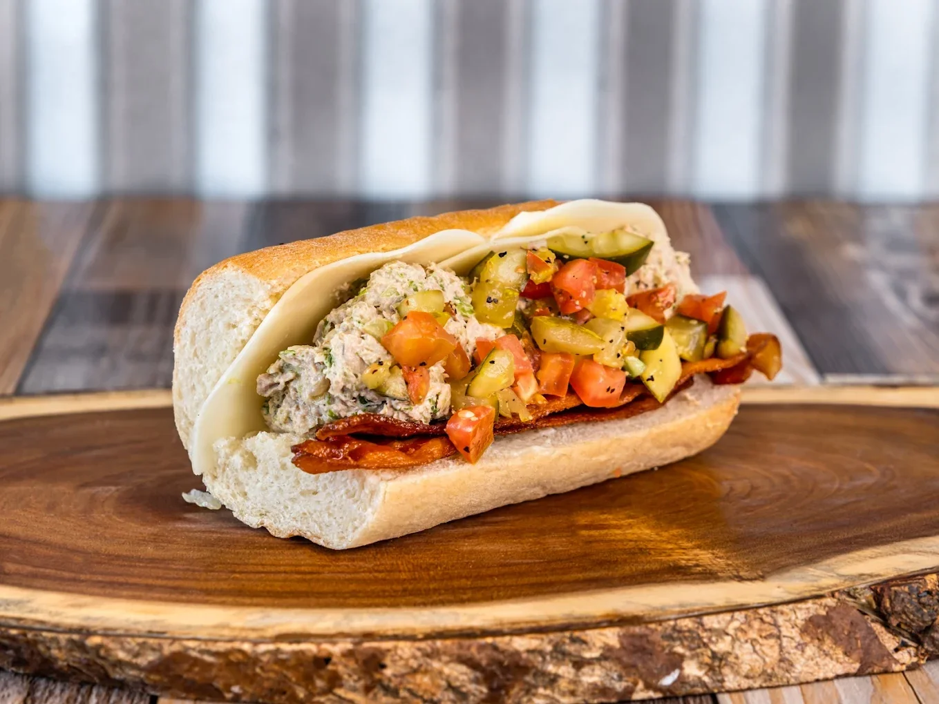 A submarine sandwich with meats, cheese, and mixed vegetables on a wooden serving board.