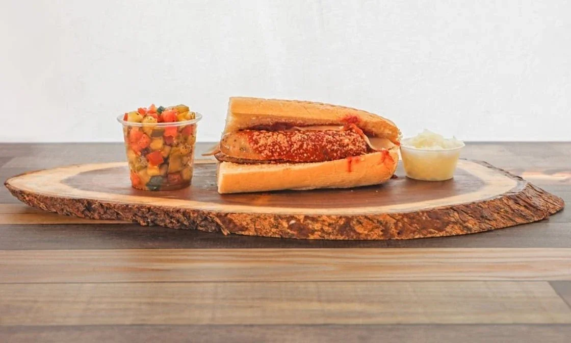 Sub sandwich with a side of potato chips and a small cup of salad on a wooden serving board.