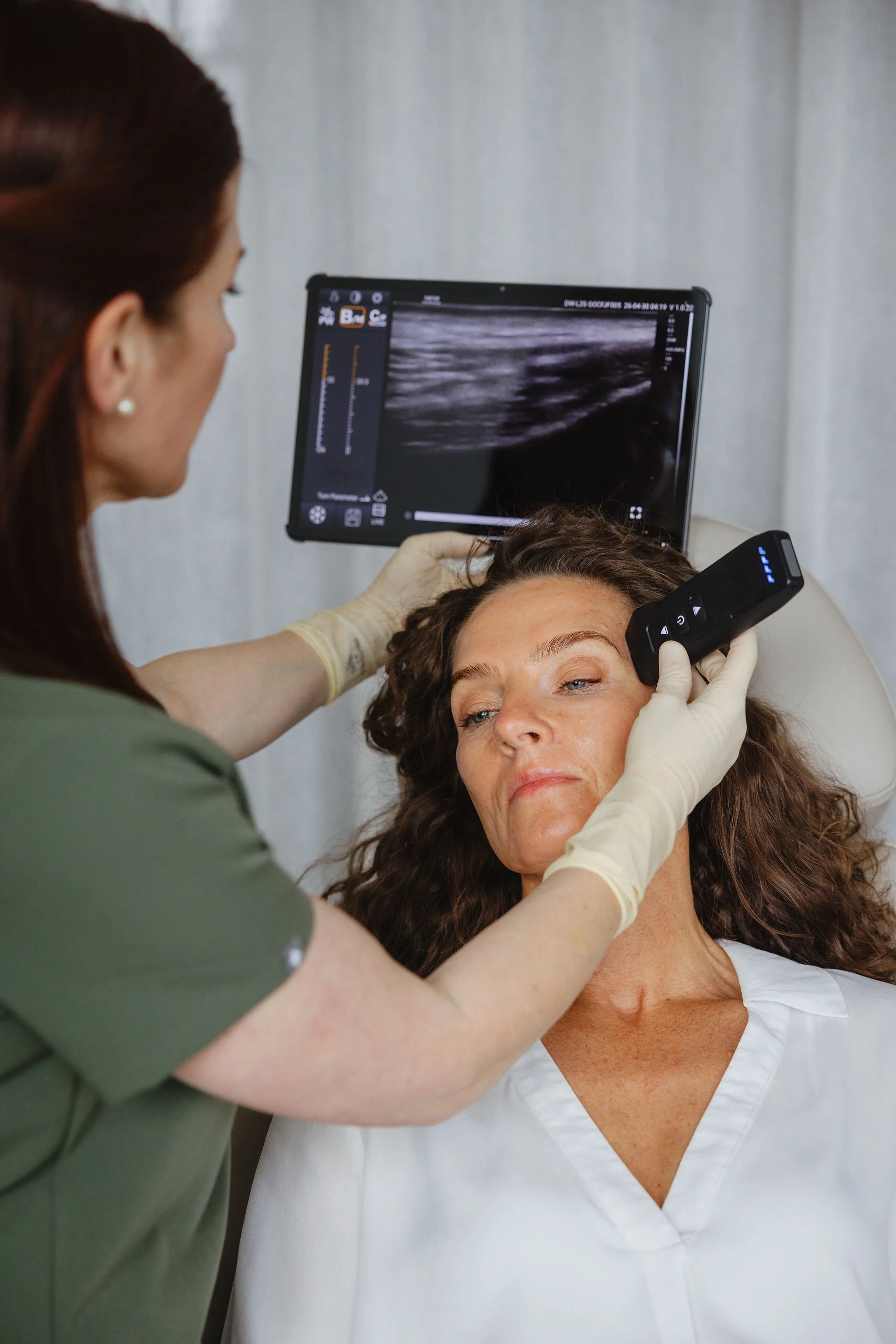 A medical professional performs an ultrasound procedure on a woman lying down, with an ultrasound monitor displaying an image in the background.